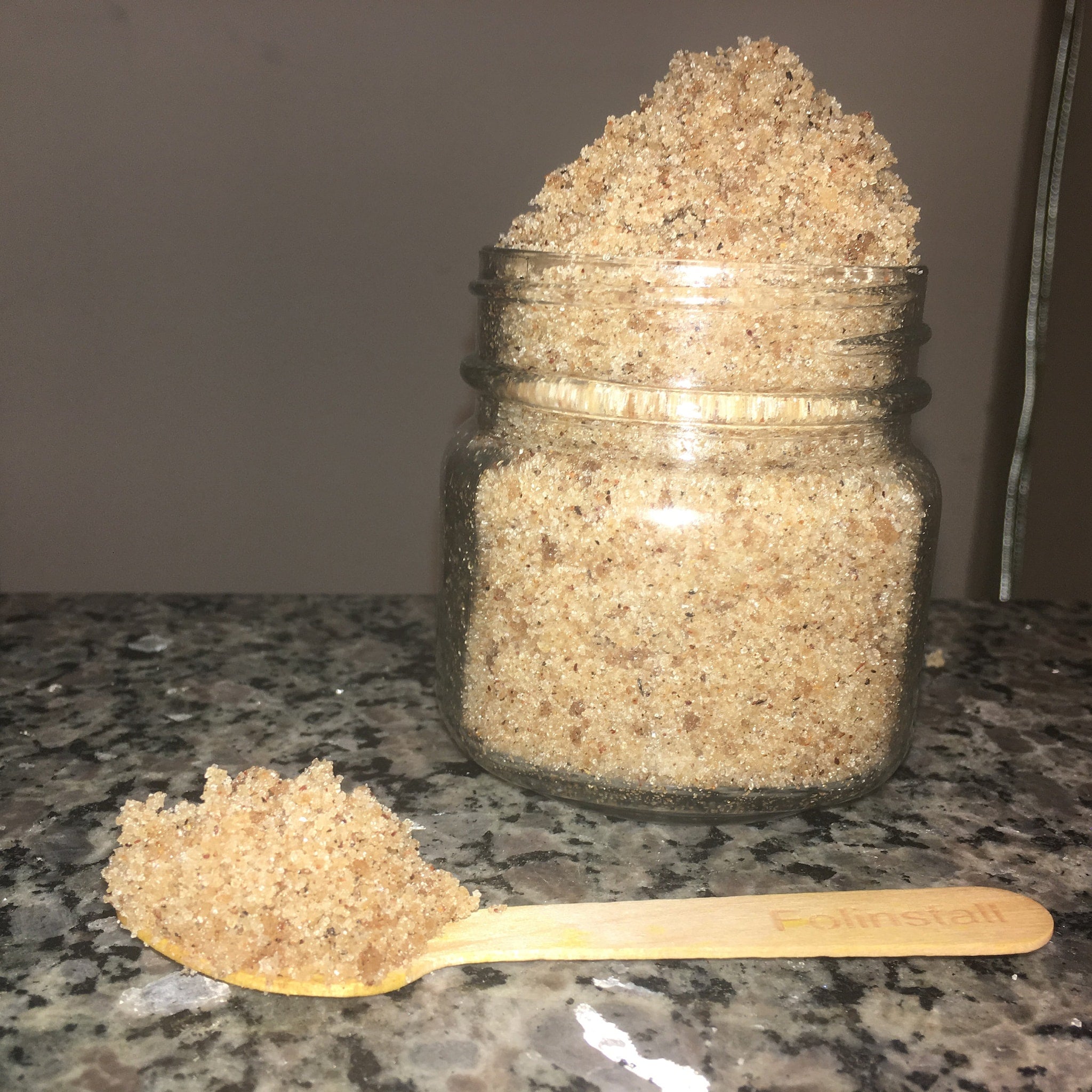 Brown granular substance in glass jar and on wooden spoon, "Folinistall" text visible