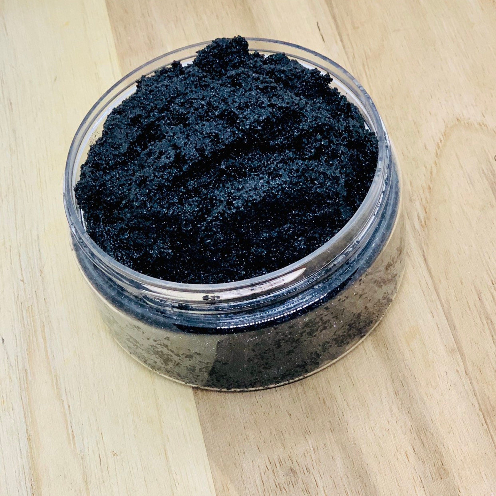 Black glitter in clear plastic jar on light wood surface