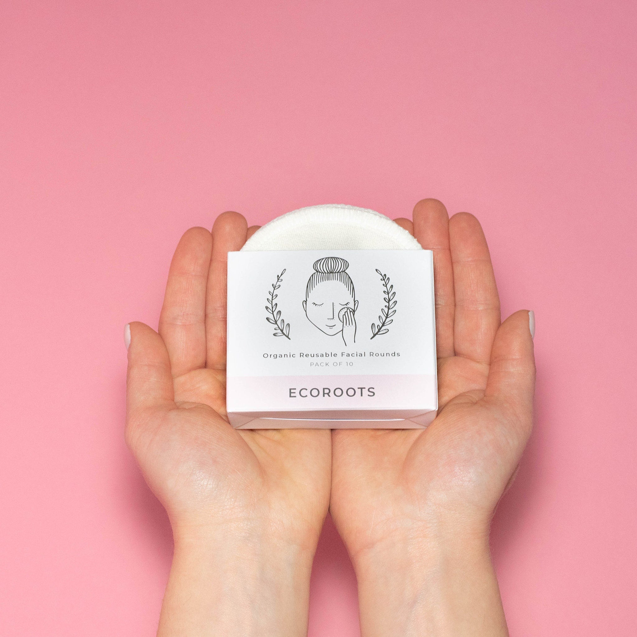 Reusable facial rounds in white box, held in hands, with Ecoroots text on pink background