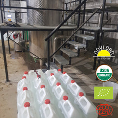 White plastic containers with red caps, stacked on concrete floor near metal stairs and tanks, New Day logo visible
