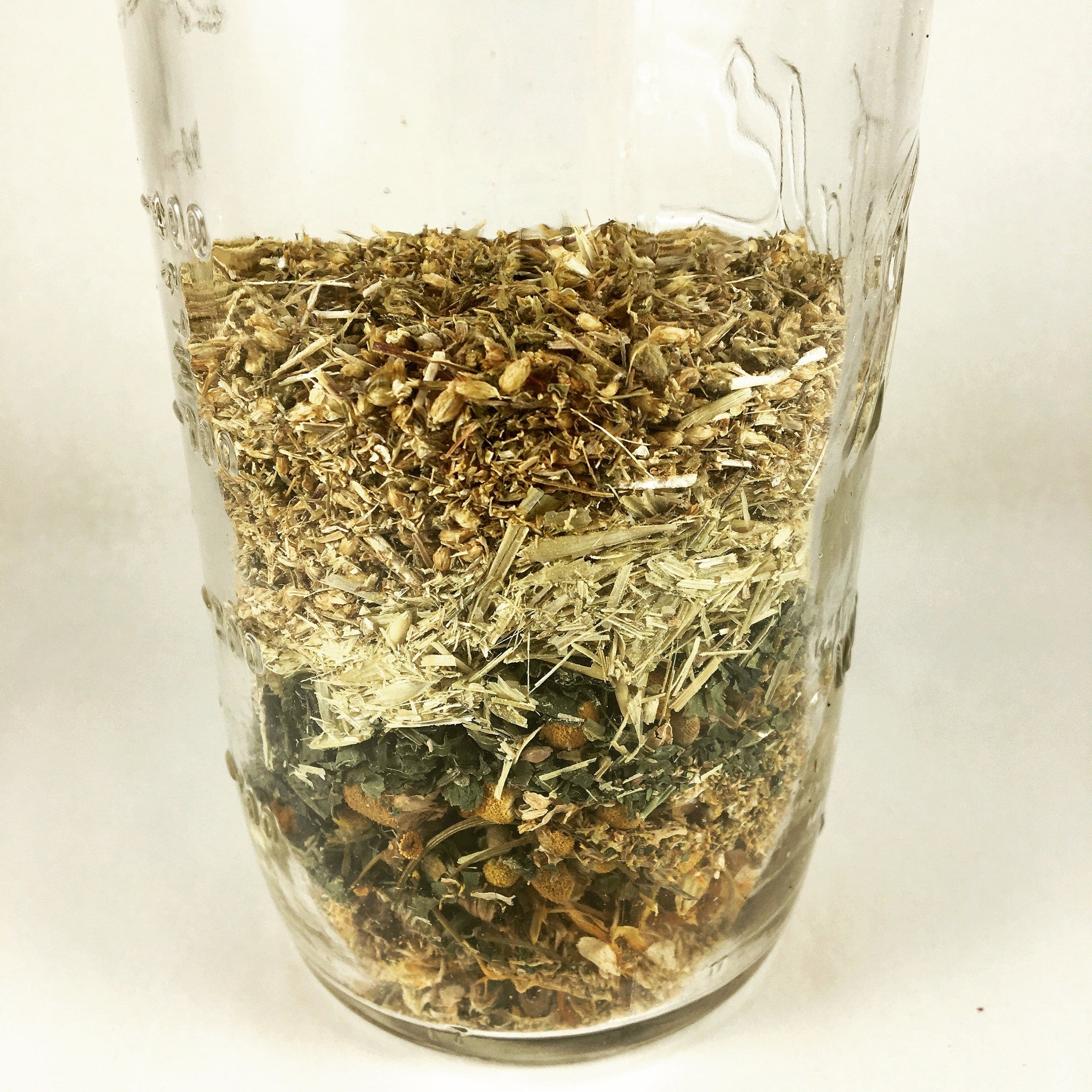 Dried herbs in clear glass jar with layers of brown, green, and tan plant matter
