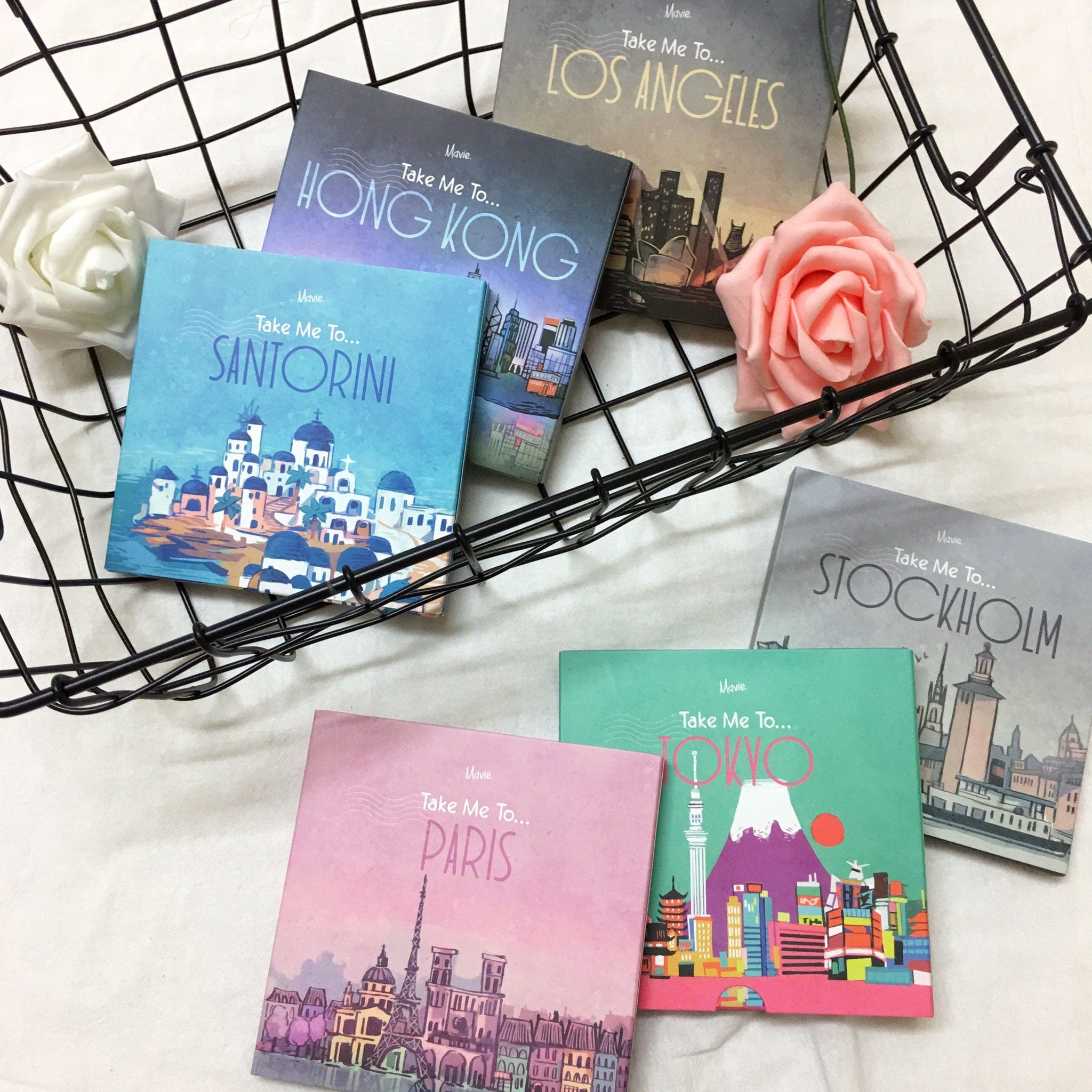 Mavie Cosmetics Take Me To eyeshadow palettes in various colors with city illustrations, in a basket