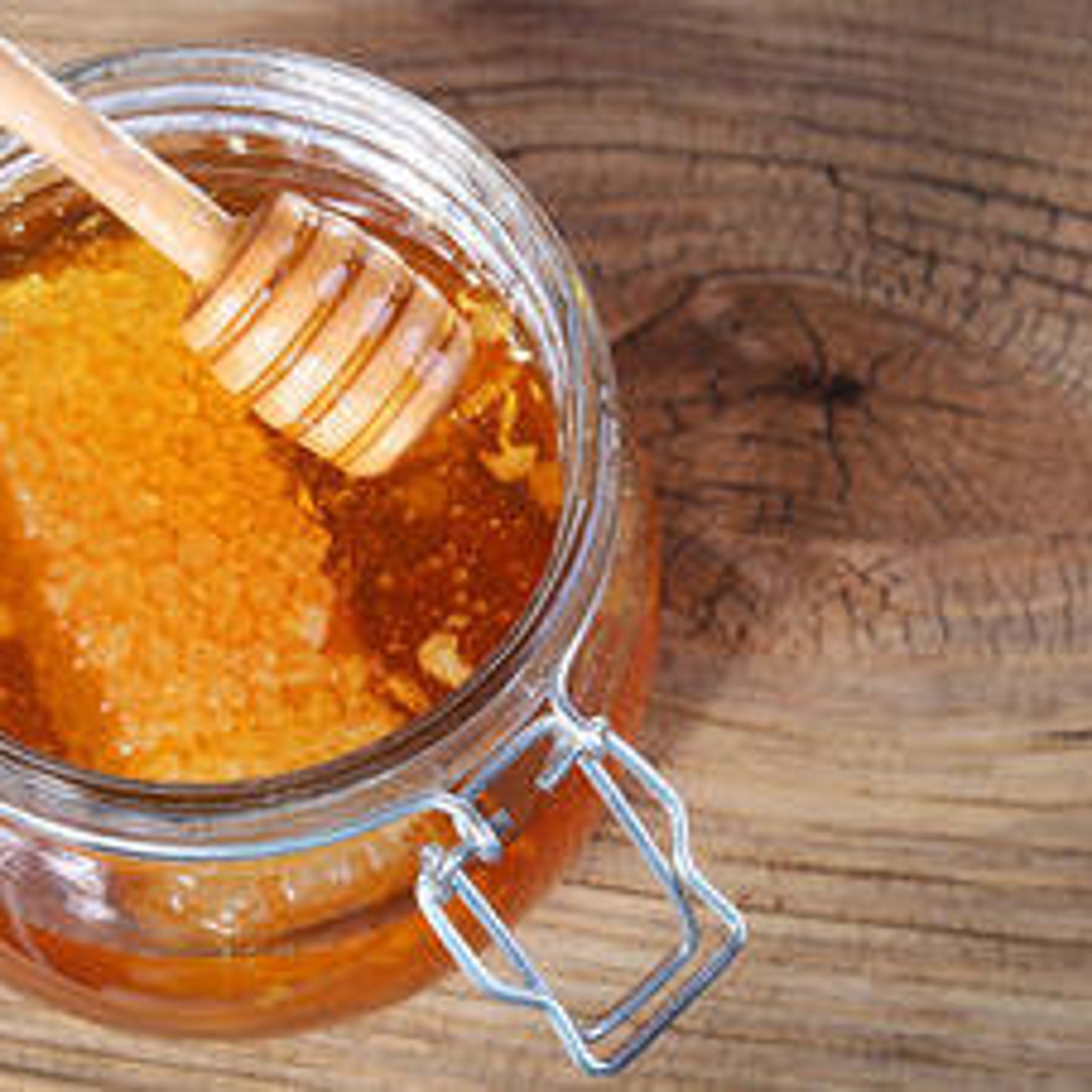 Honey in glass jar with wooden dipper, amber liquid and wooden background.