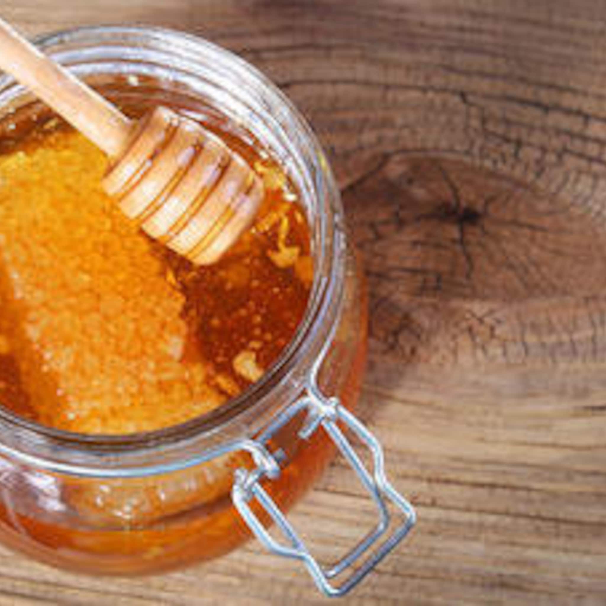 Honey in jar with wooden dipper, amber liquid, glass jar, on wood surface