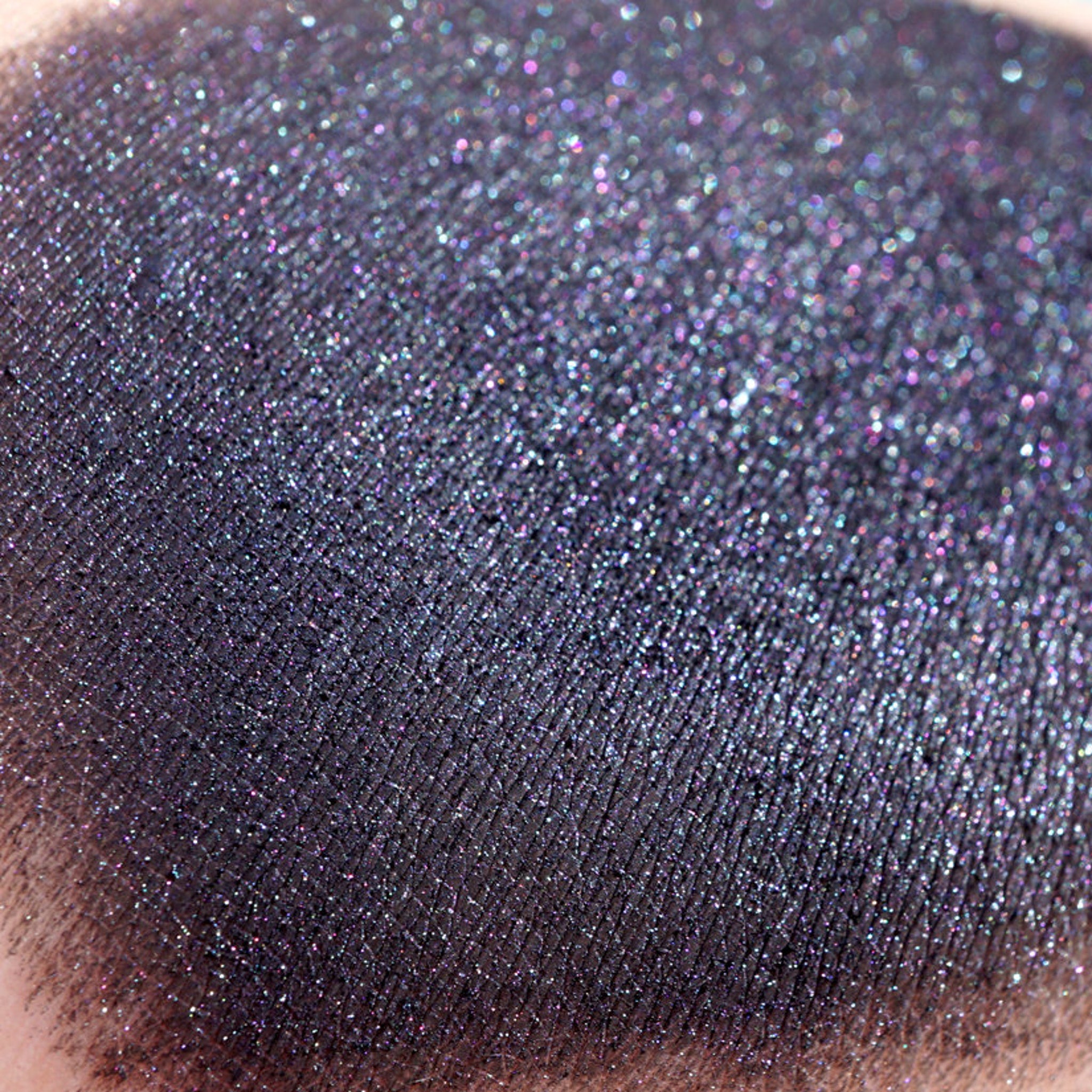 Side view of loose metallic black eye shadow with iridescent gunmetal shimmer in a minimalist jar
