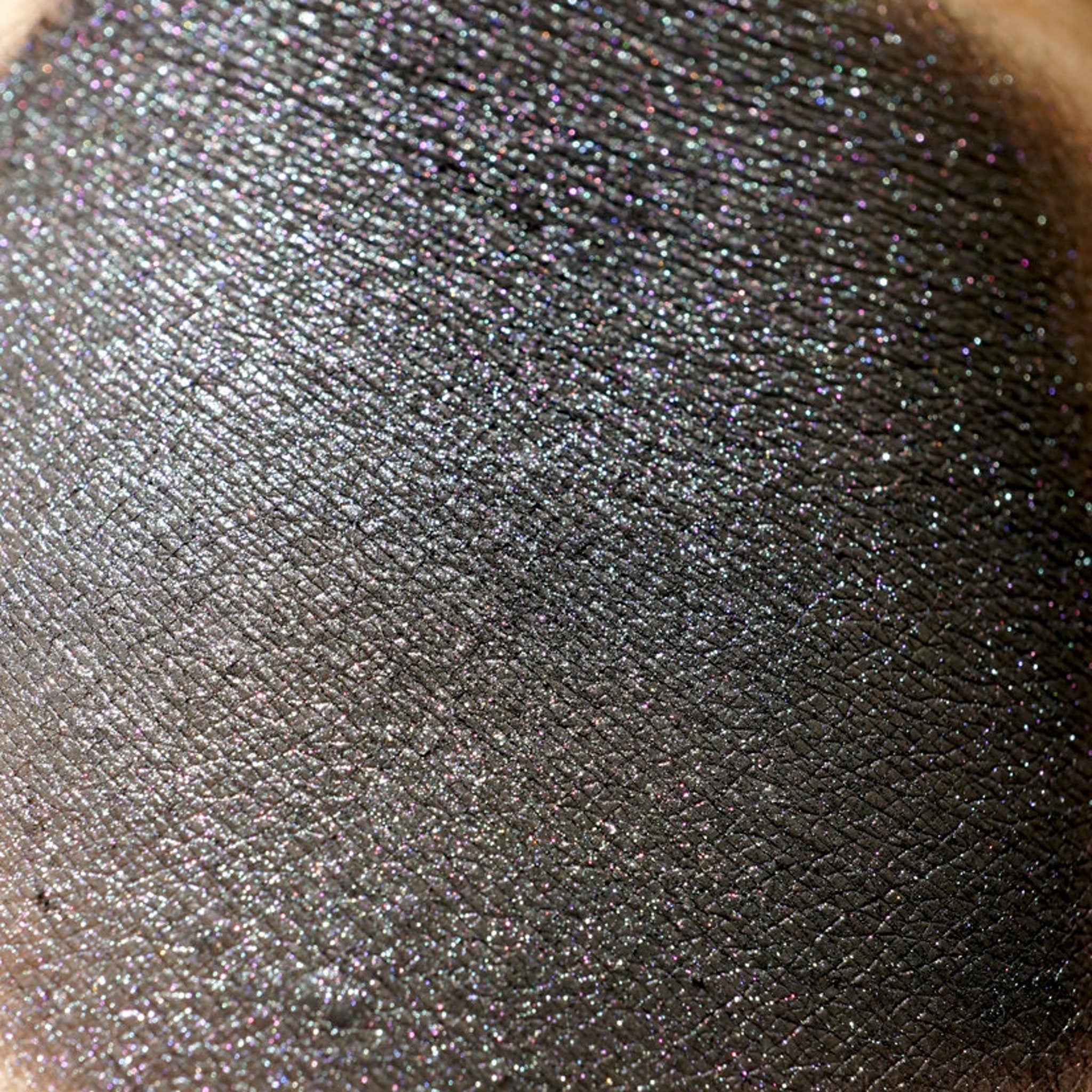 Side view of loose metallic black eye shadow with iridescent gunmetal shimmer in a small glass jar