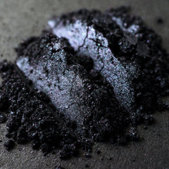 Side view of loose metallic black eye shadow with iridescent gunmetal shimmer in minimalist jar packaging