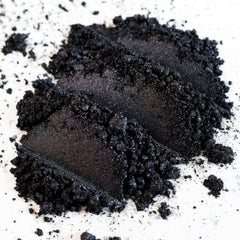 Close-up of loose metallic black eye shadow with iridescent gunmetal shimmer particles sparkling in light
