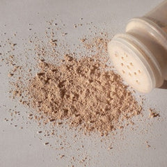 Loose powder beige color spilled from a clear plastic container on a white surface