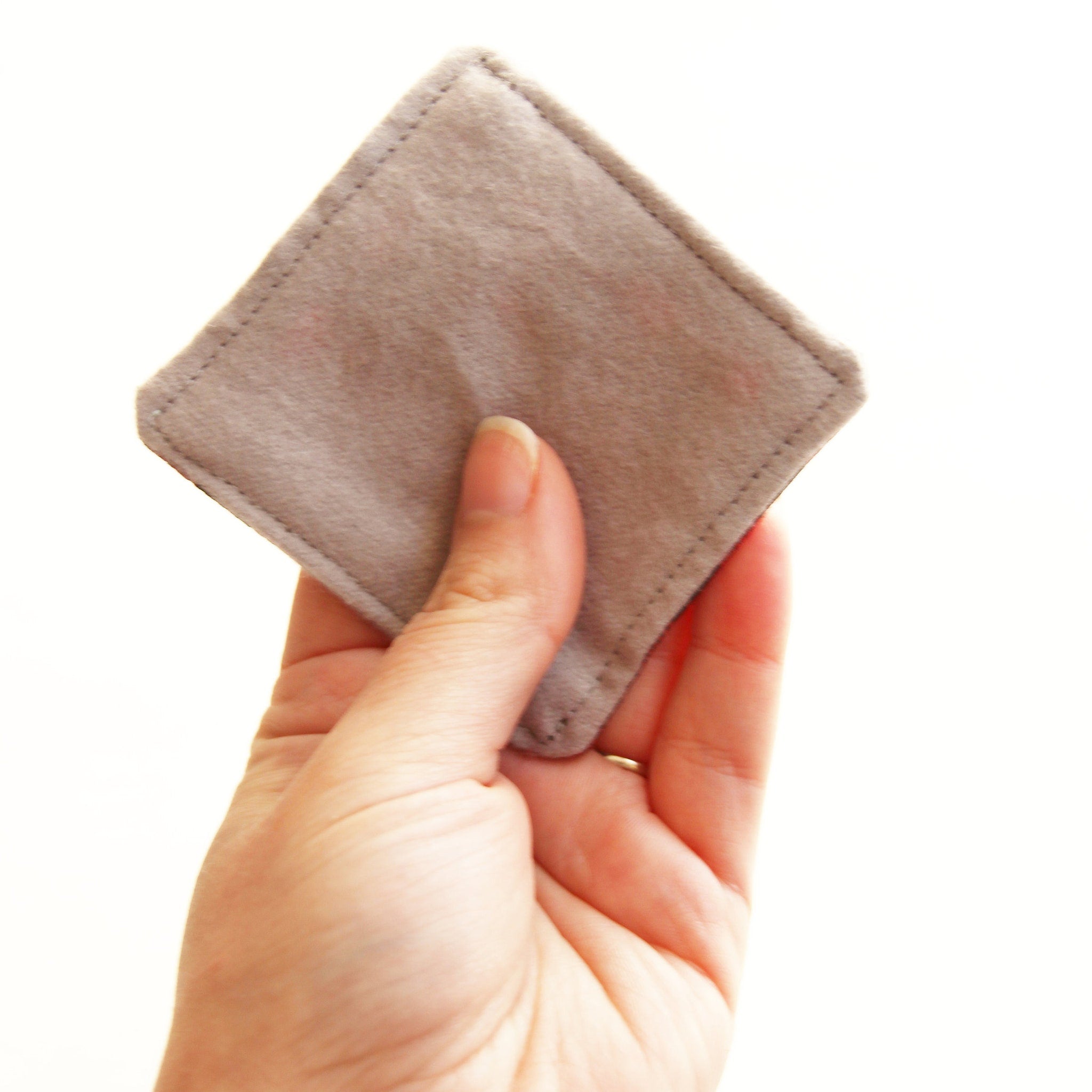 Square gray fabric pad held in hand with stitched edges
