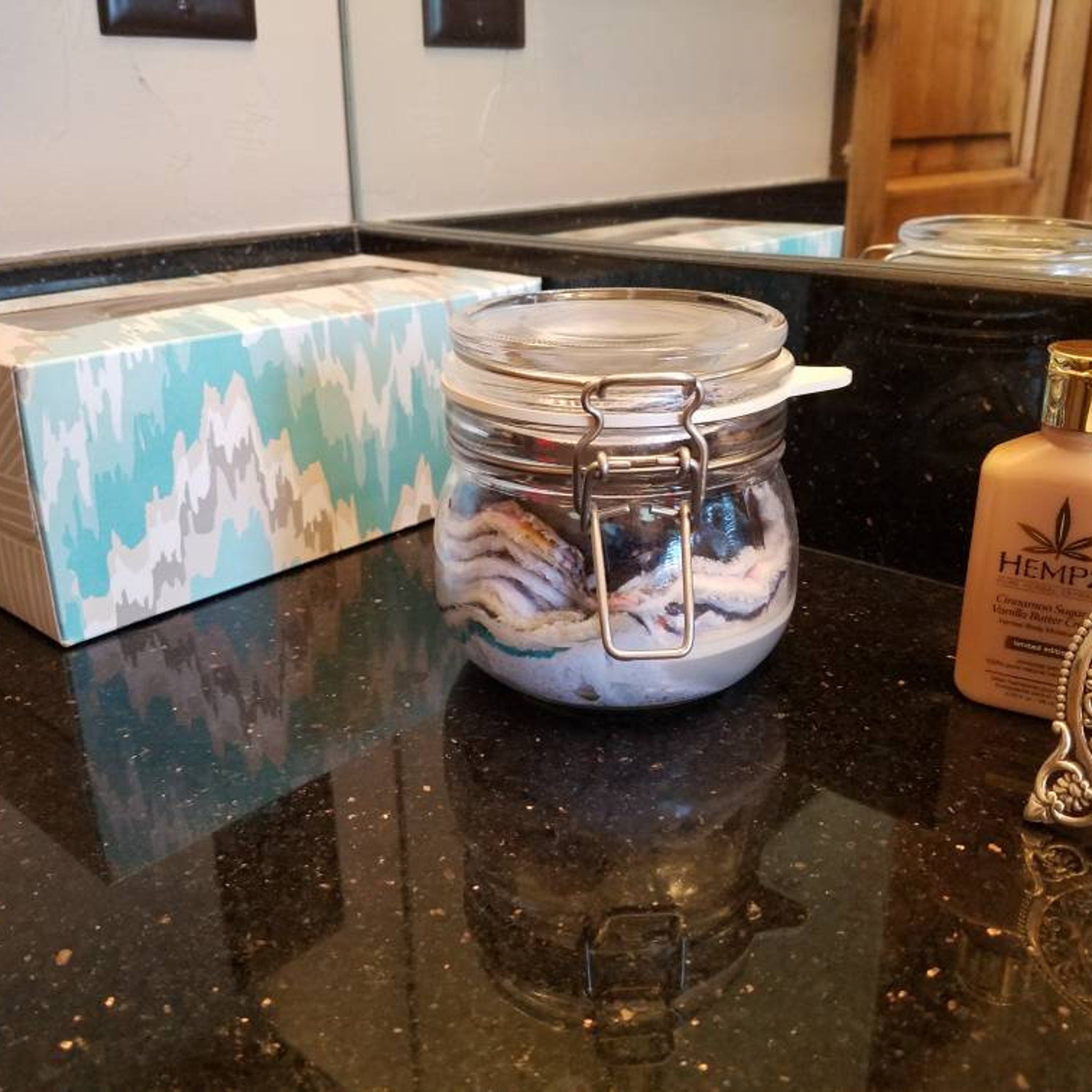 Glass jar with silver clasp, clear glass, containing white and purple items on countertop