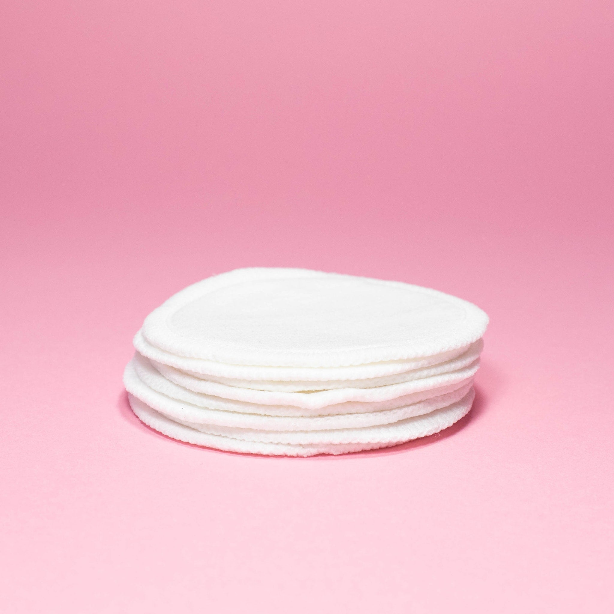 Reusable cotton pads, white circular fabric pads stacked on pink background