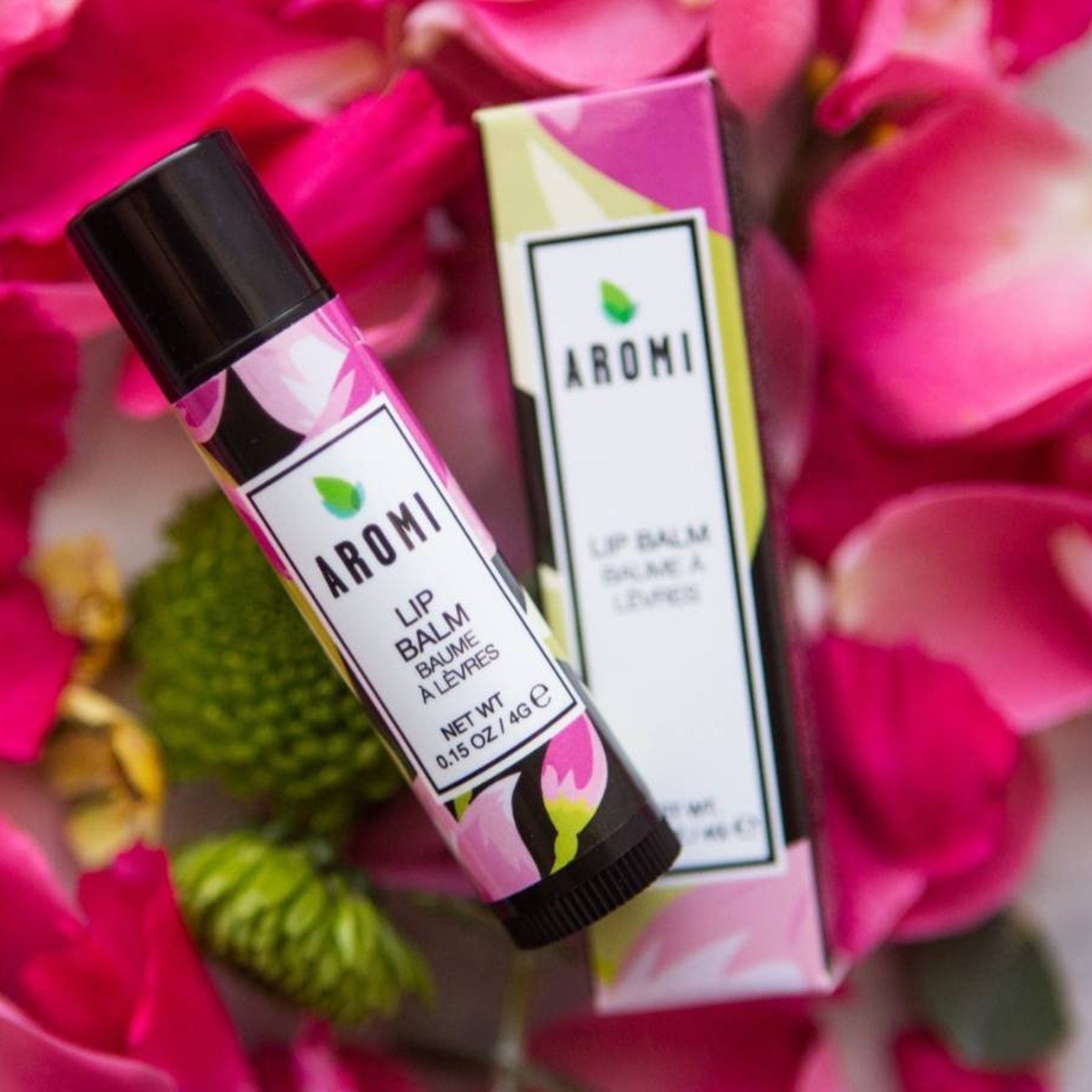 Lip balm tube with black cap and floral pattern, AROMI brand packaging, surrounded by pink petals