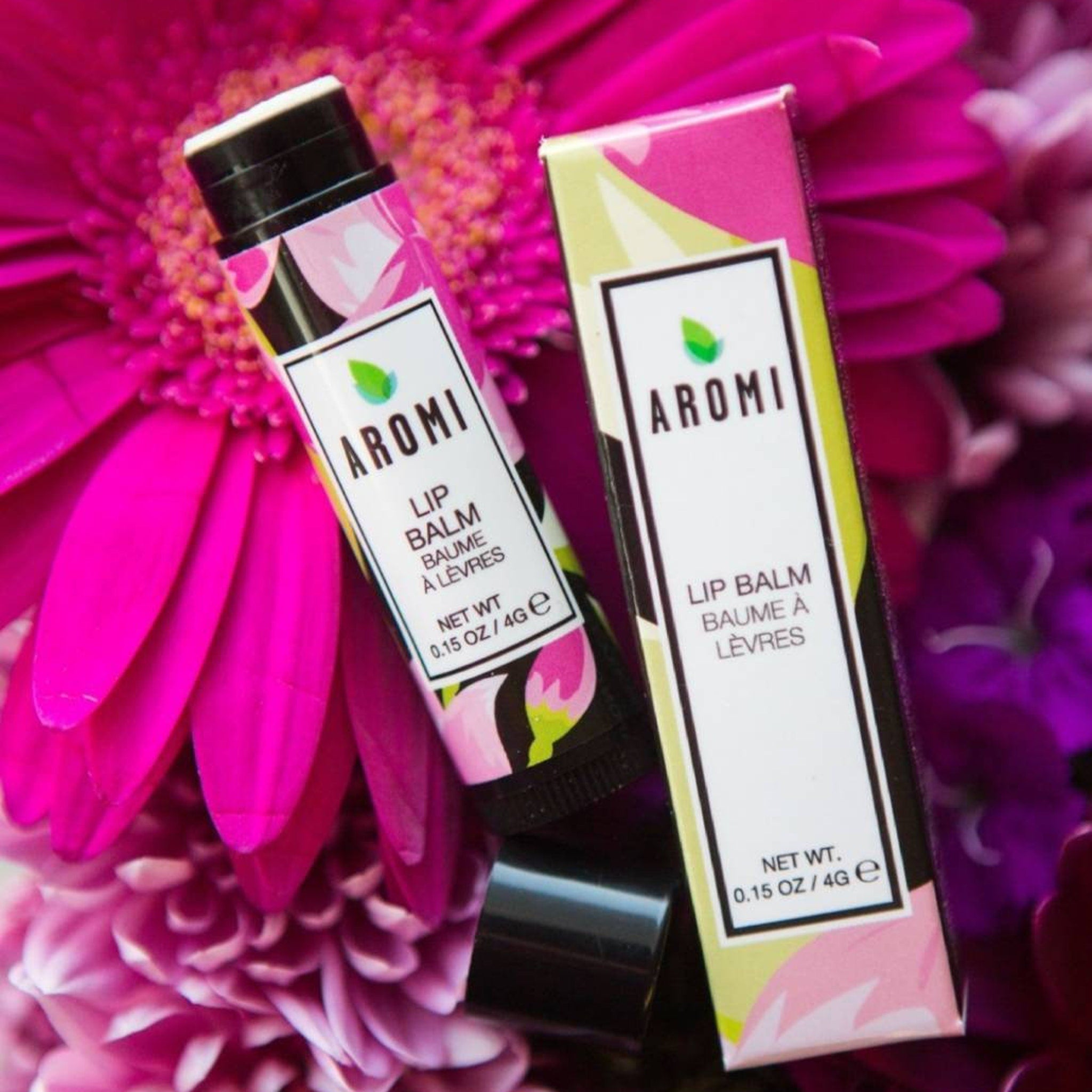 Lip balm tube with pink floral pattern, black cap, and "AROMI" branding on white label next to box