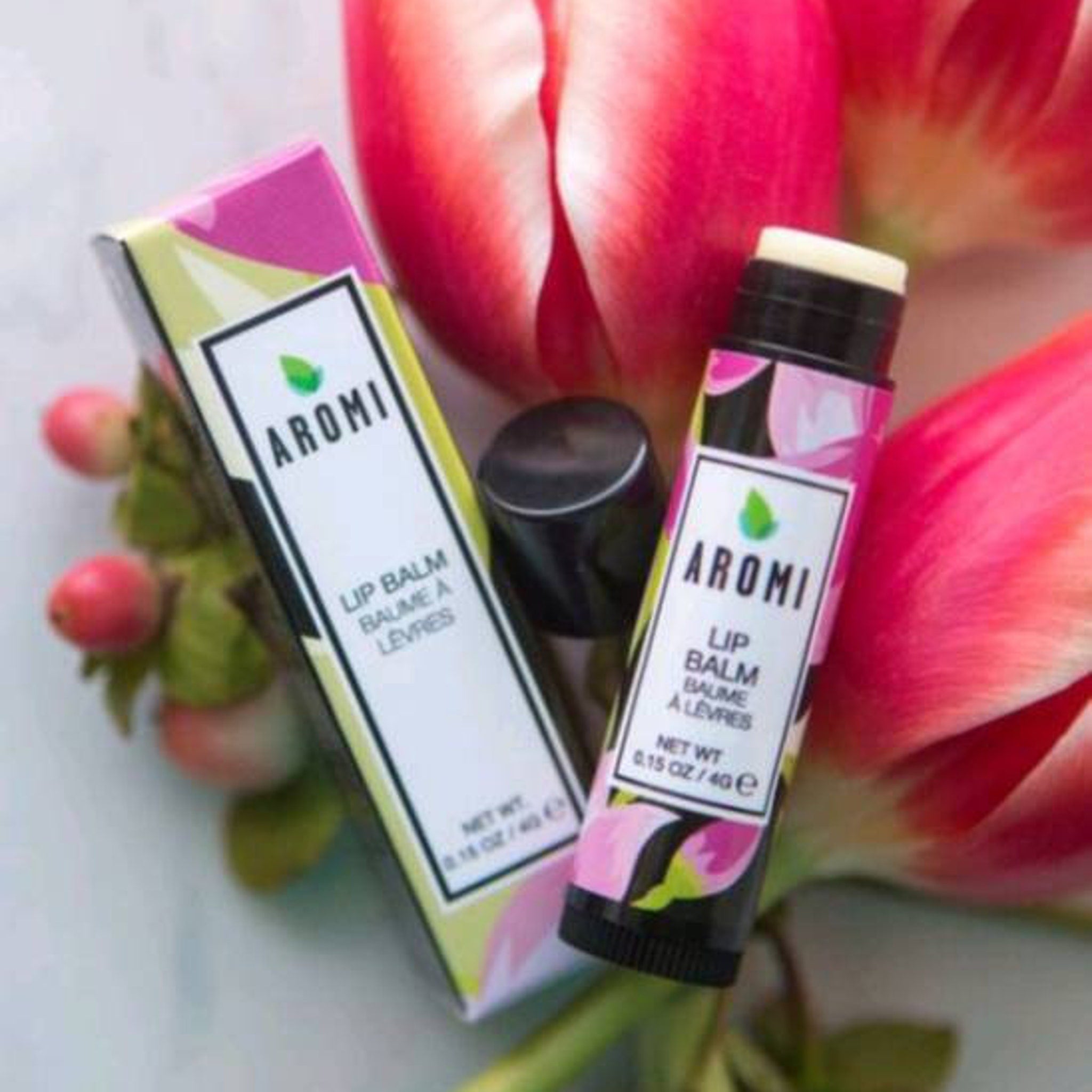Lip balm with pink floral pattern, black cap, and "AROMI" text, near flowers