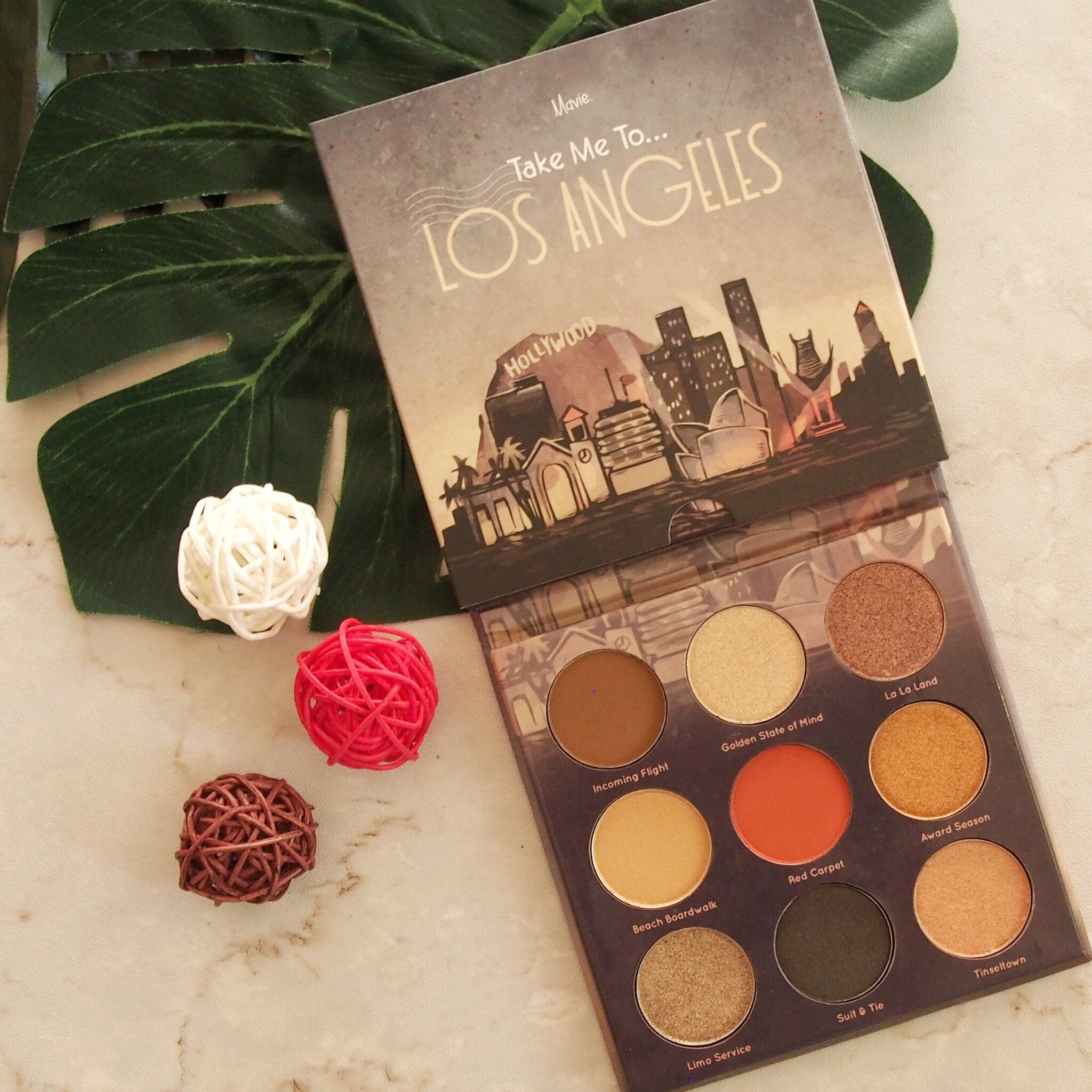 Eyeshadow palette with Mavie Cosmetics branding, multi-color shades, and Los Angeles theme on a marble surface