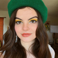 Green beret with wavy brown hair, yellow eyeshadow, and orange lipstick on a person's face