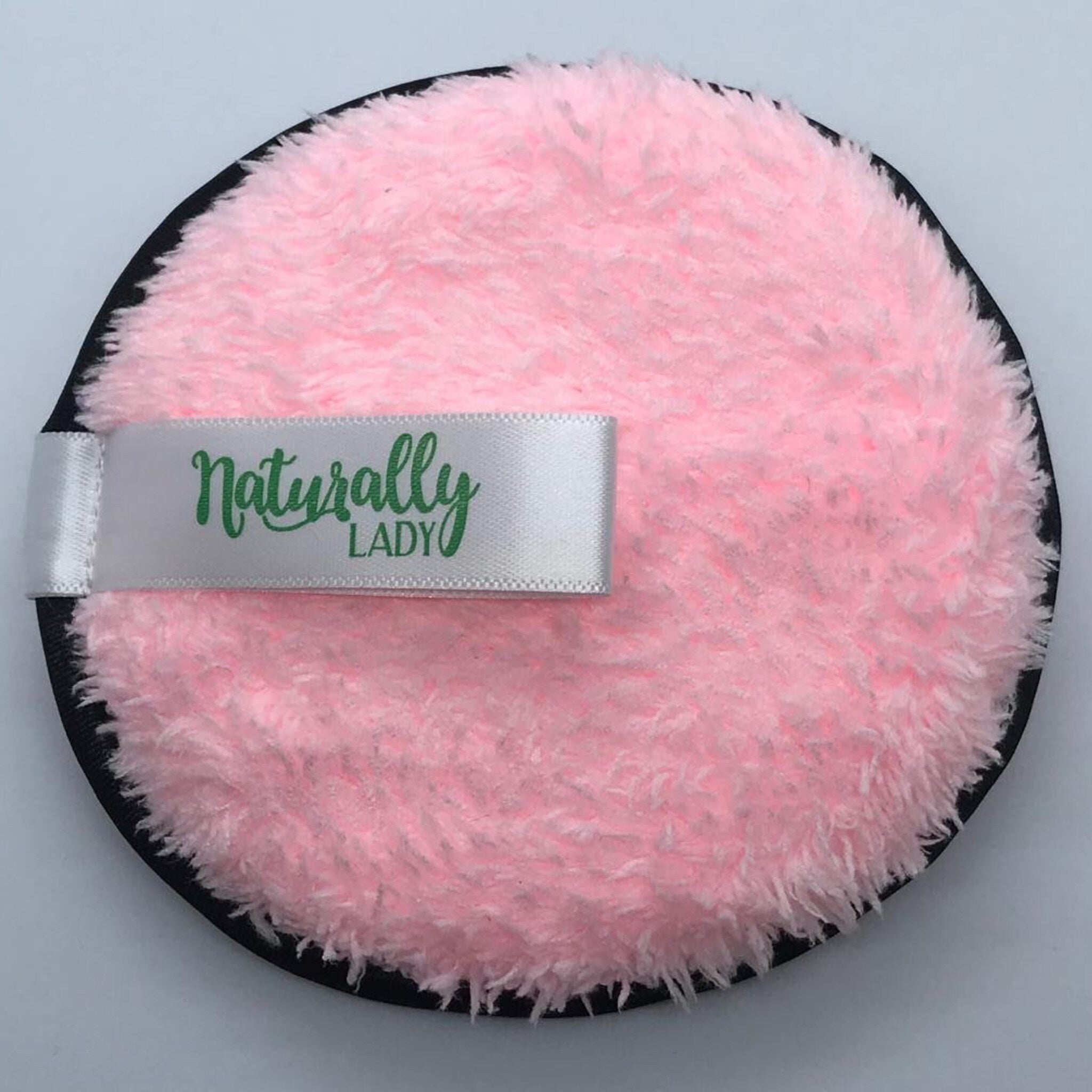 Makeup remover pad with pink fluffy material, black trim, and white Naturally Lady ribbon