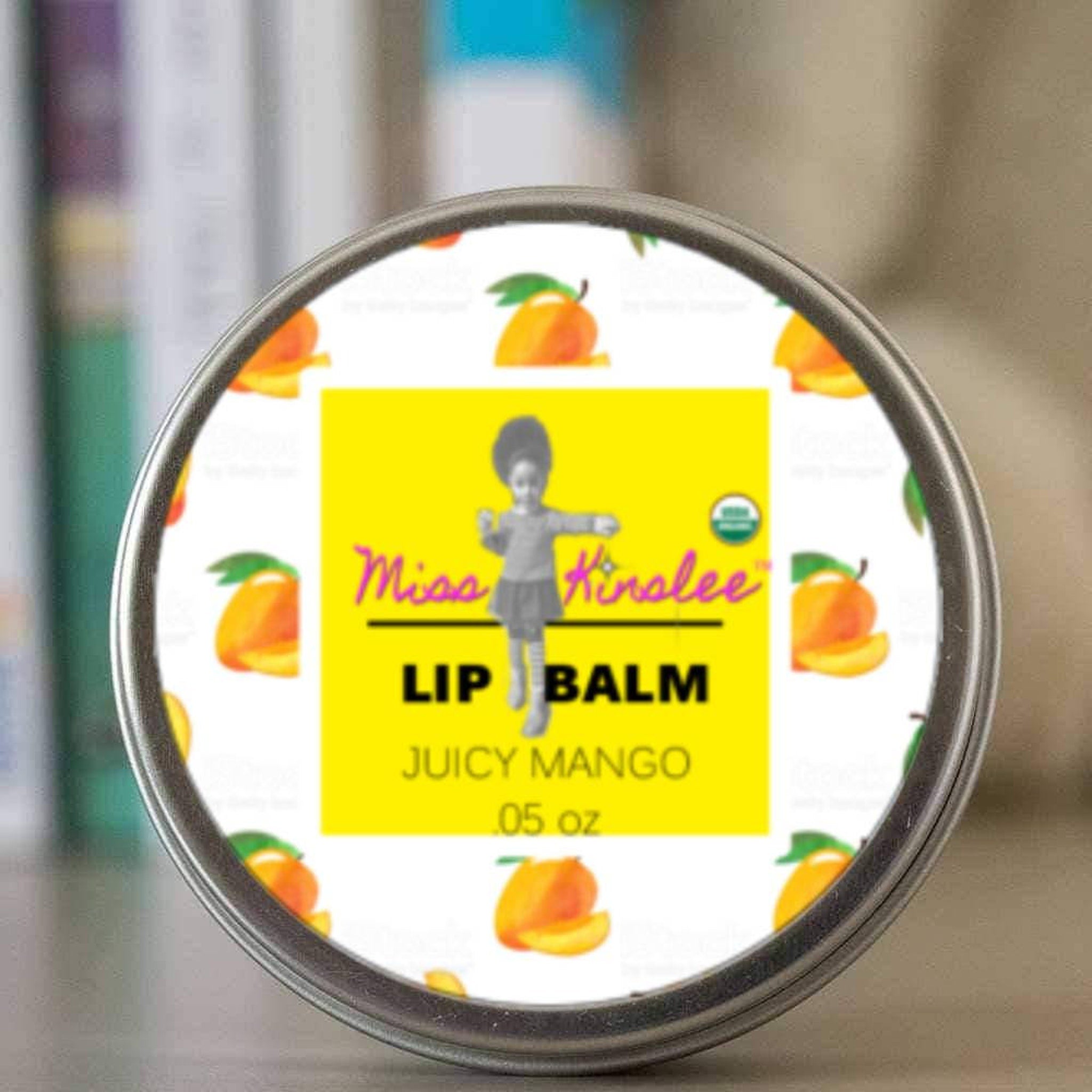 Lip balm tin with mango pattern, yellow label, and Miss Kinslee text