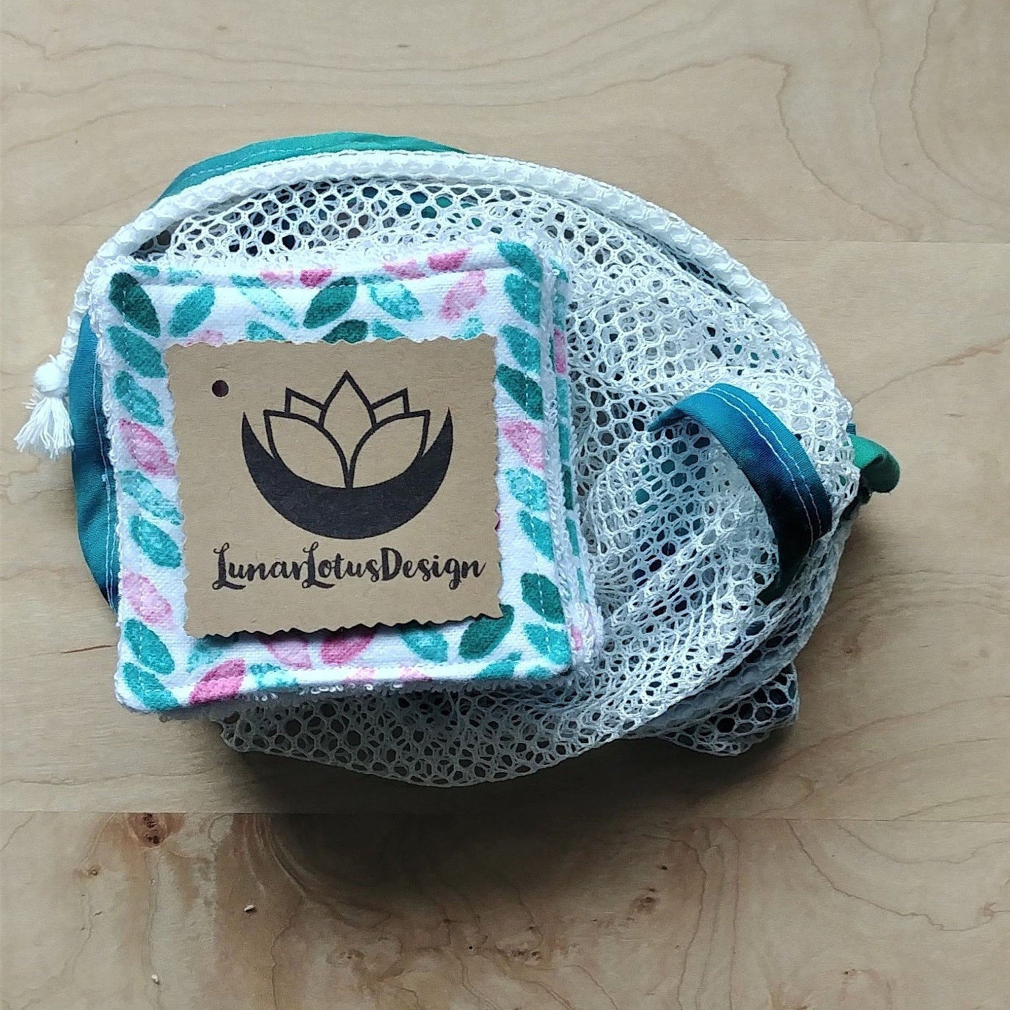 Reusable face rounds with green and pink leaf pattern, white mesh bag, Lunar Lotus Design tag on wooden surface