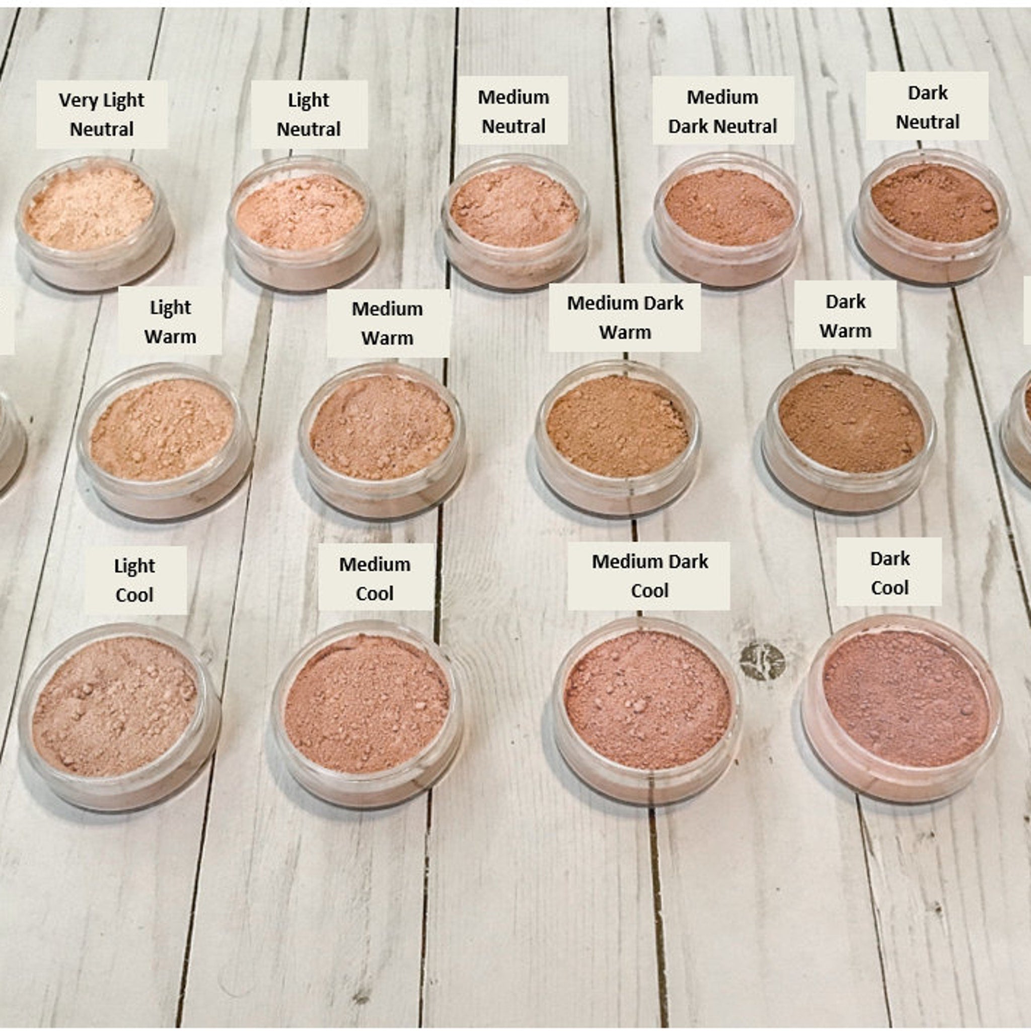 Powder makeup in various shades of beige, pink, and brown, in clear plastic jars on a wooden surface