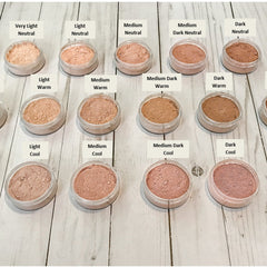 Powder makeup in various shades of beige, pink, and brown, in clear plastic jars on a wooden surface