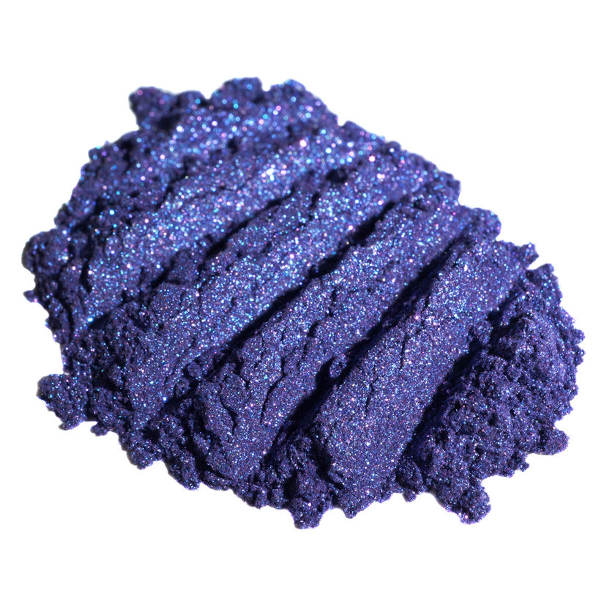 Hand applying dark purple loose pigment eyeshadow with shifting indigo glitter onto eyelid
