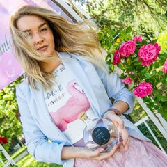 Rose water bottle held by woman, clear glass bottle with cork, black label with "TRAKE ROSE" text
