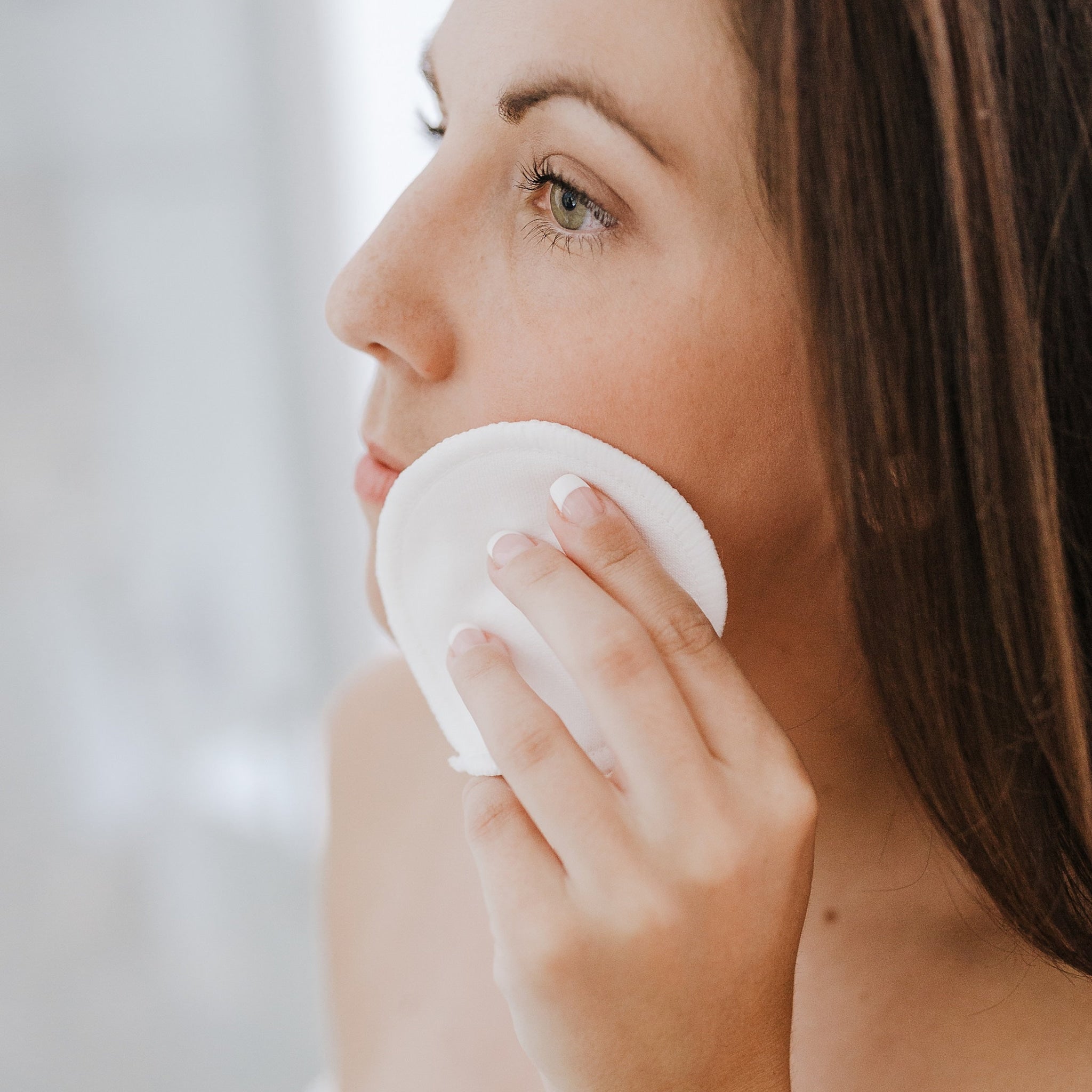 Reusable cotton pad, white circular pad, held to face, for skincare routine