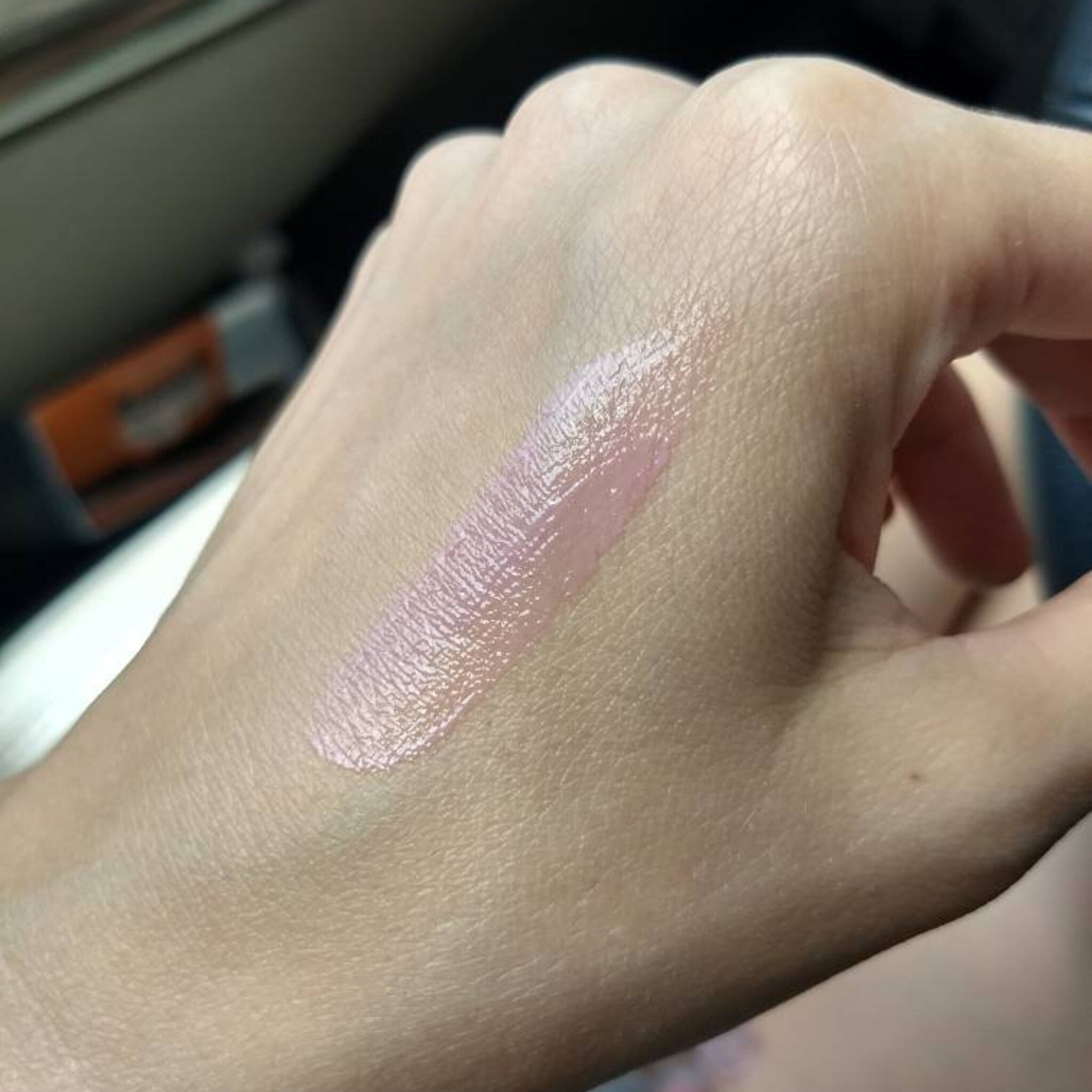 Lip gloss swatch, pink glossy texture on skin, applied on hand