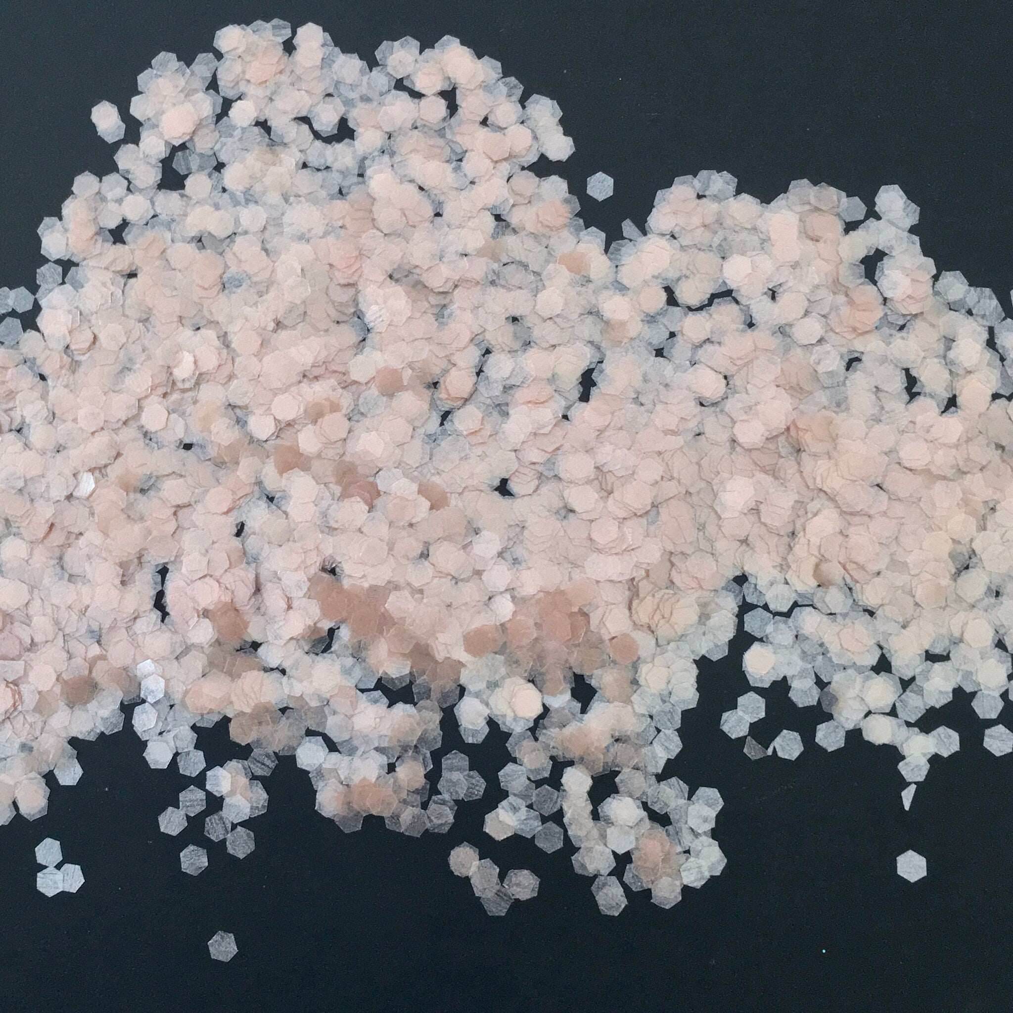 Glitter flakes in hexagonal shape, light pink and white, scattered on black background