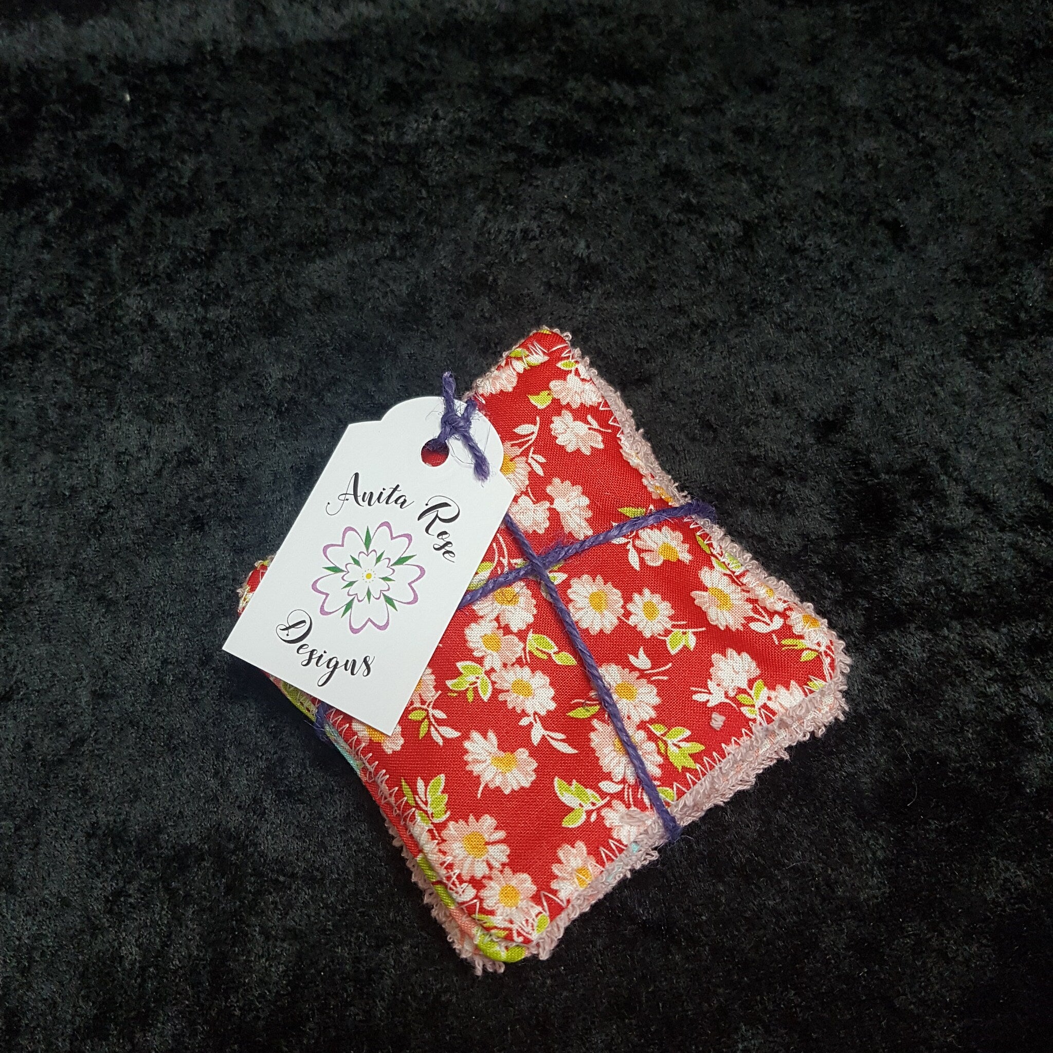 Red floral fabric squares with white daisy pattern, pink trim, and Anita Rose Designs tag