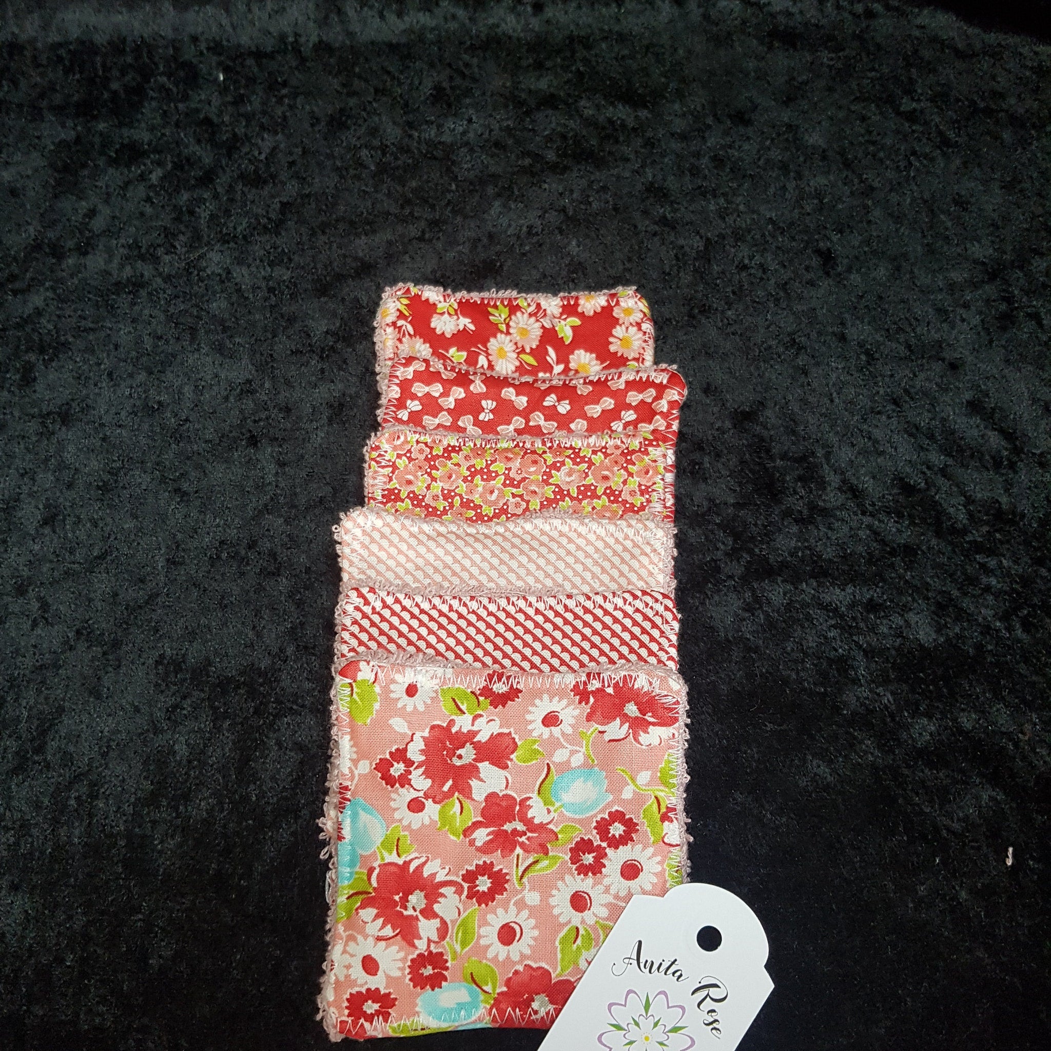 Fabric squares with red floral, pink and white patterns, and white stitching, Anita Rose tag visible