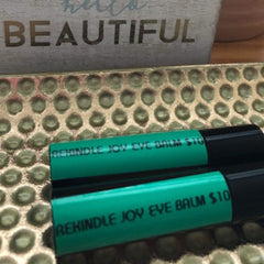 Eye balm tubes, green and black, with REKINDLE JOY text, resting on gold tray
