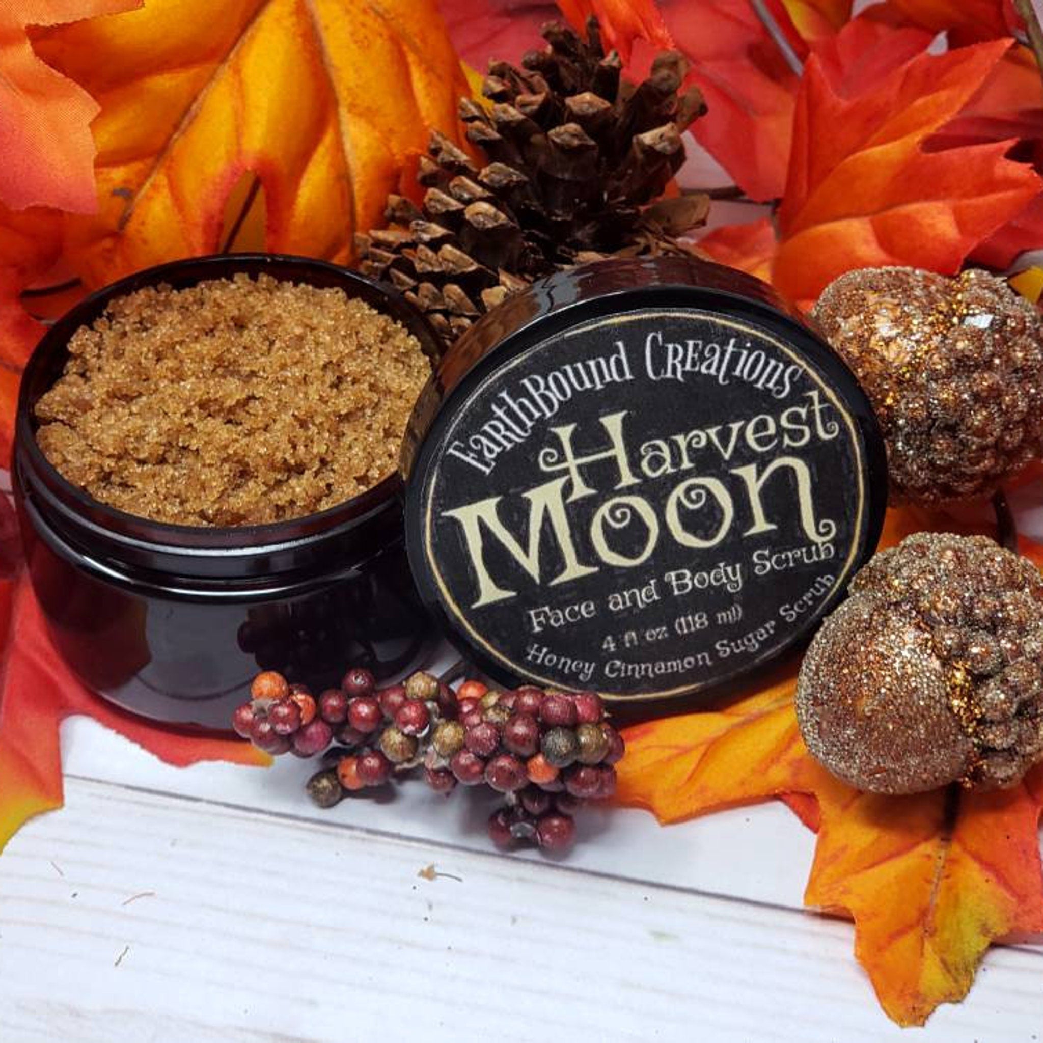 Sugar scrub in black jar with brown granules, Harvest Moon label, and fall foliage