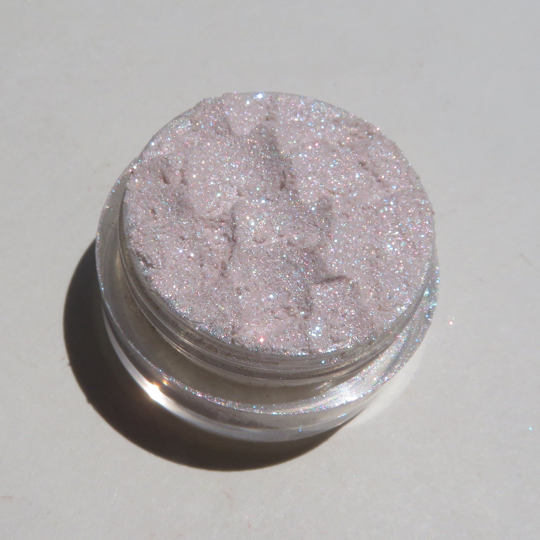 Close-up of sheer pink sparkly glitter eyeshadow with shimmer particles on fingertips
