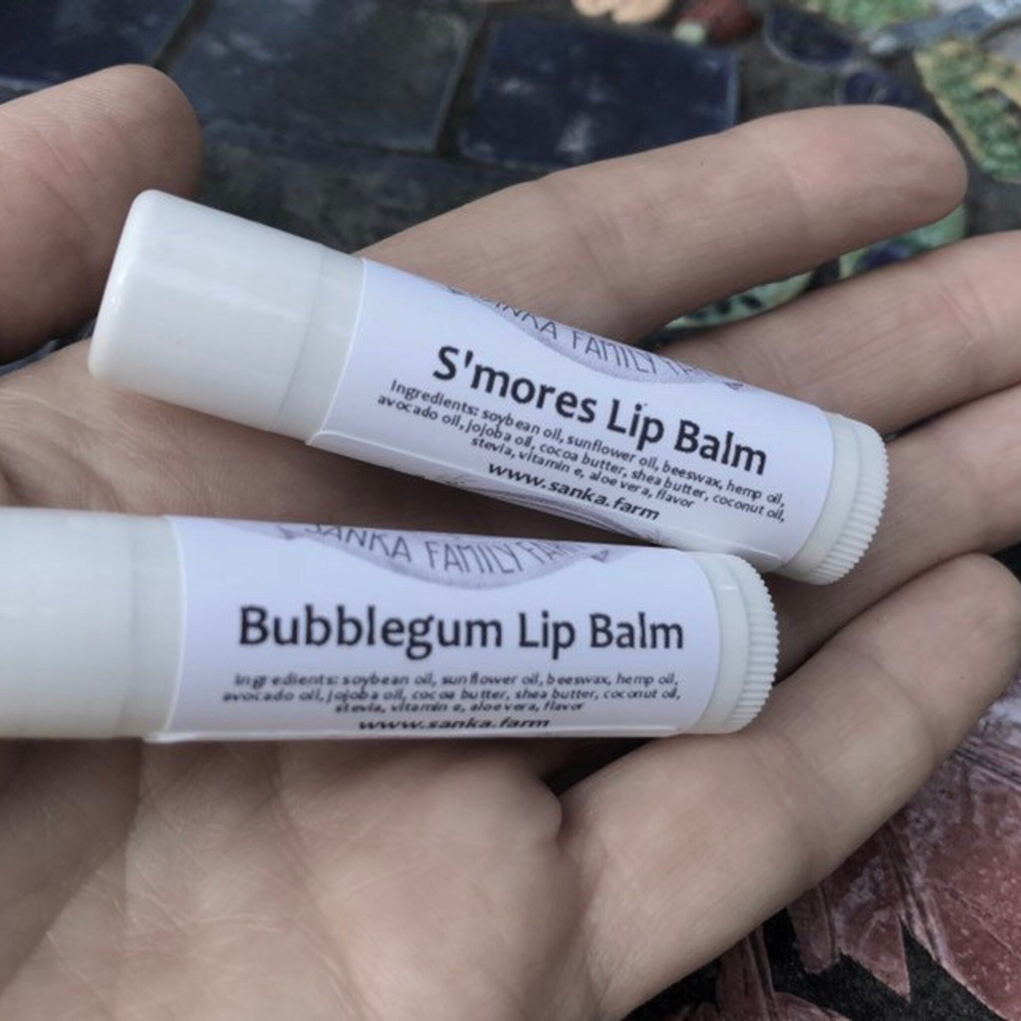 Lip balm tubes, white with printed label, held in hand, Sanka Family Farm branding visible