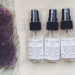Hydrosol mist bottles with black caps, clear glass, and white labels on a textured surface.