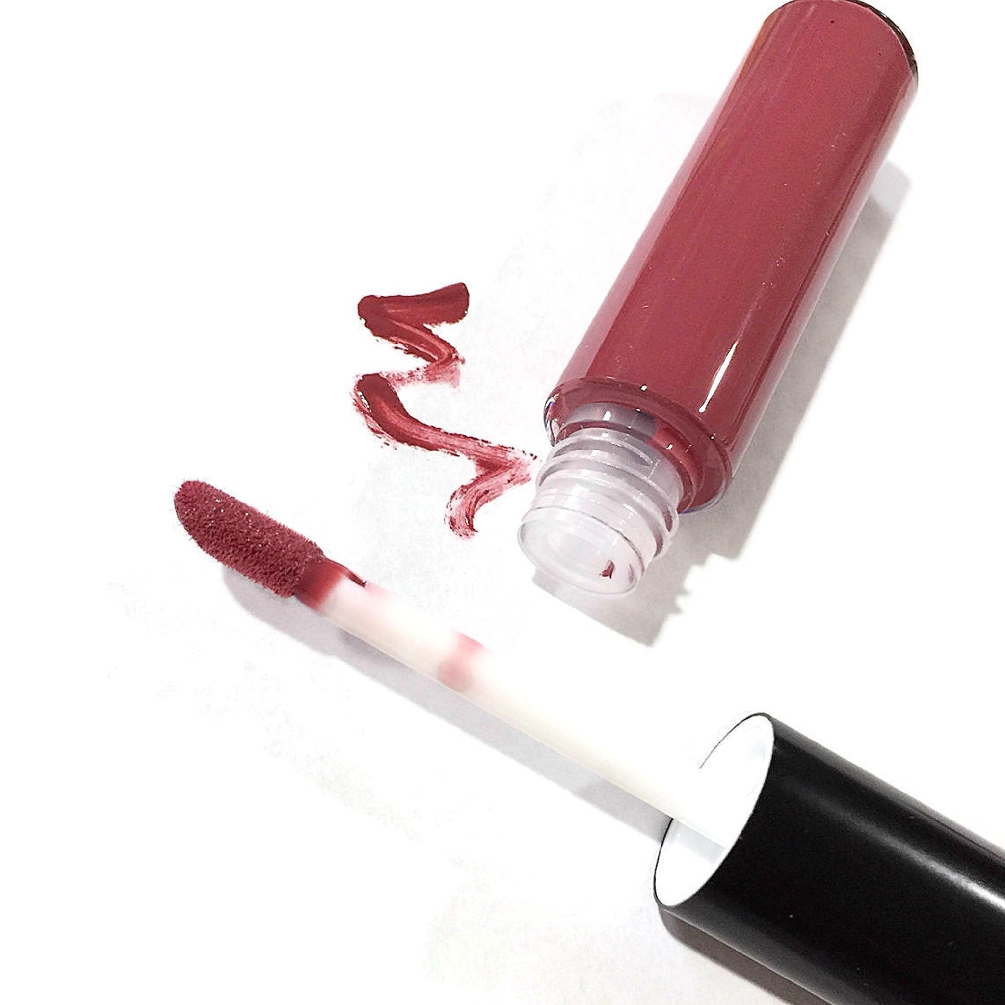 Lip gloss tube with maroon liquid, white applicator, and black cap on white surface