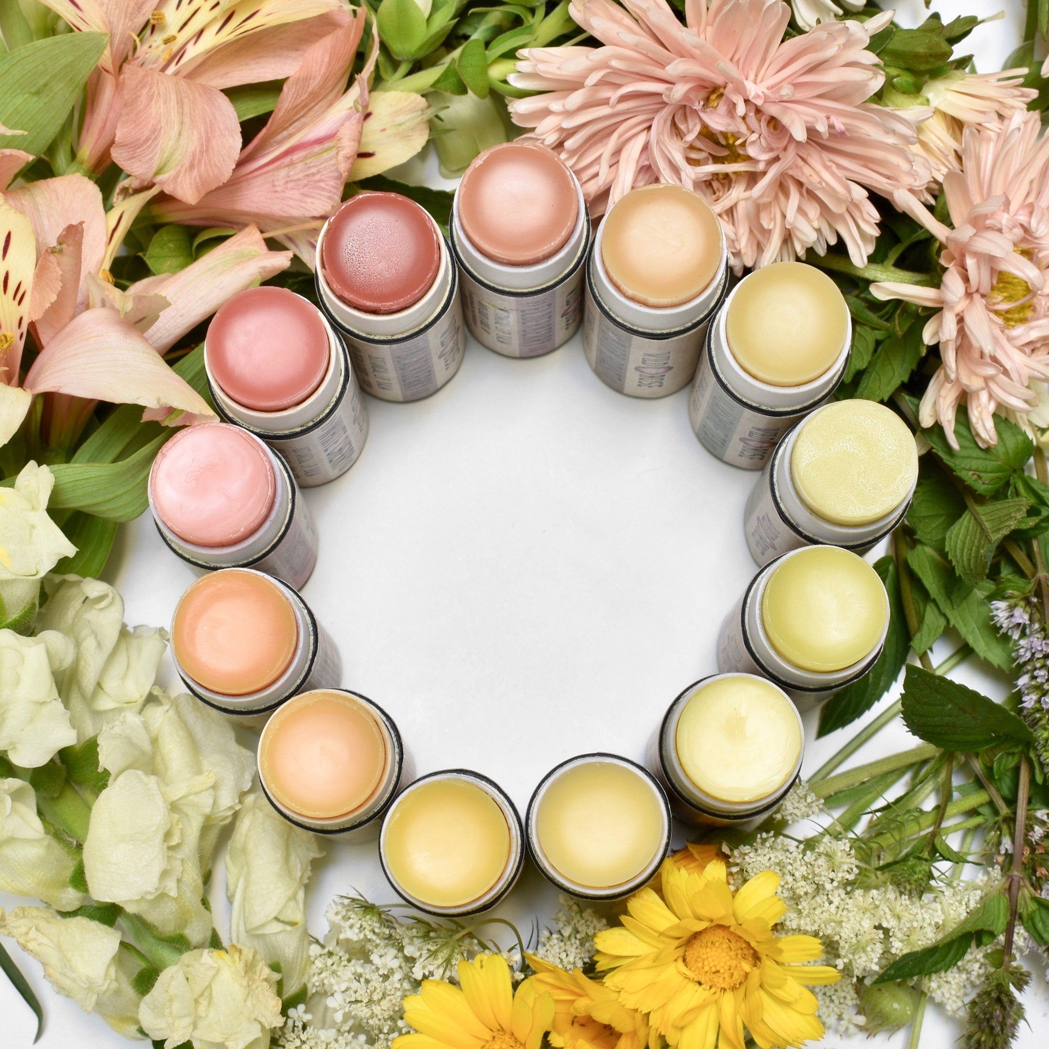 Lip balms in various colors, arranged in a circle, surrounded by flowers and greenery, Wild Rose brand visible