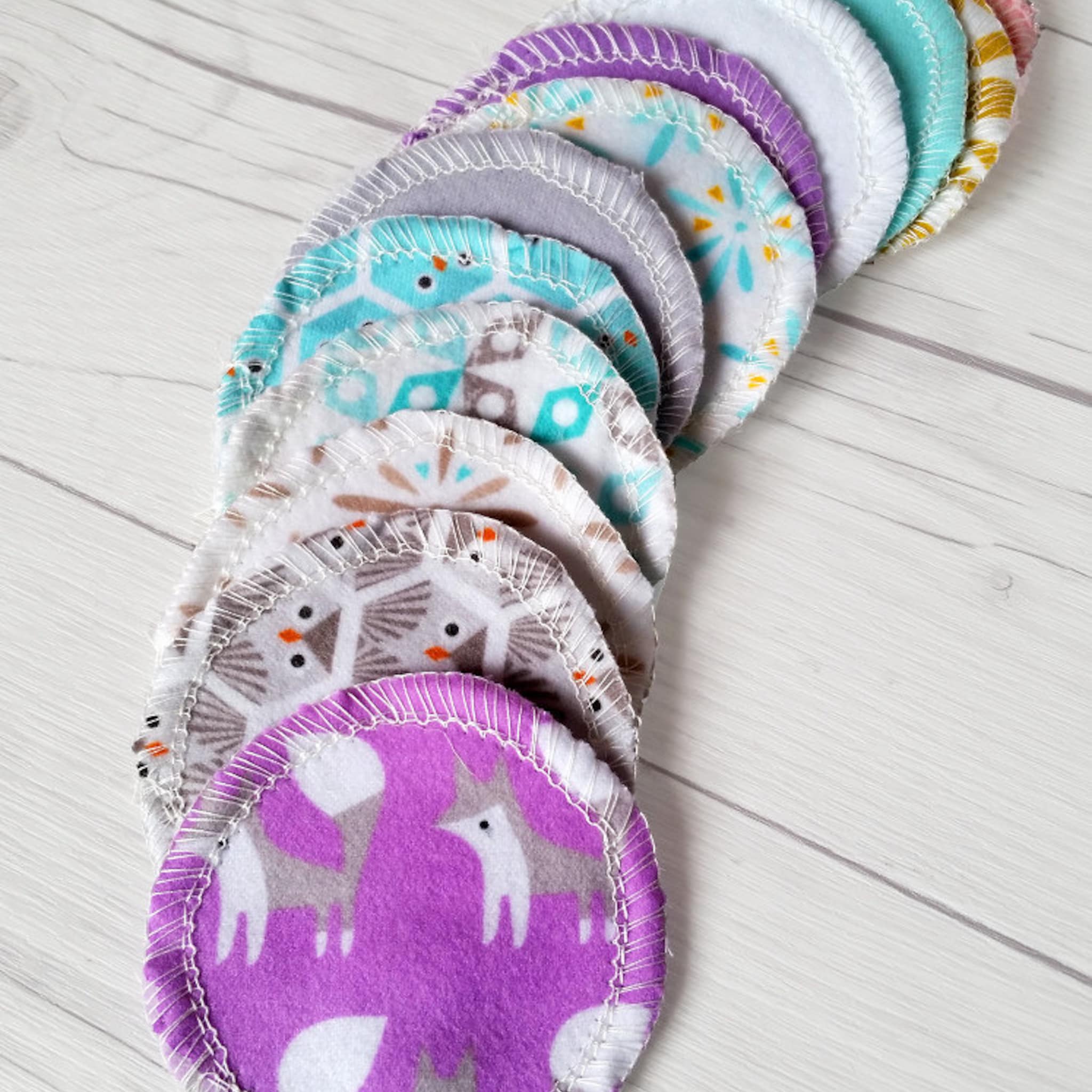 Reusable nursing pads with various patterns, colors, and white stitching around the edges.