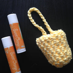 Lip balm tubes with orange label and "Sweet Orange" text, next to a yellow crocheted pouch