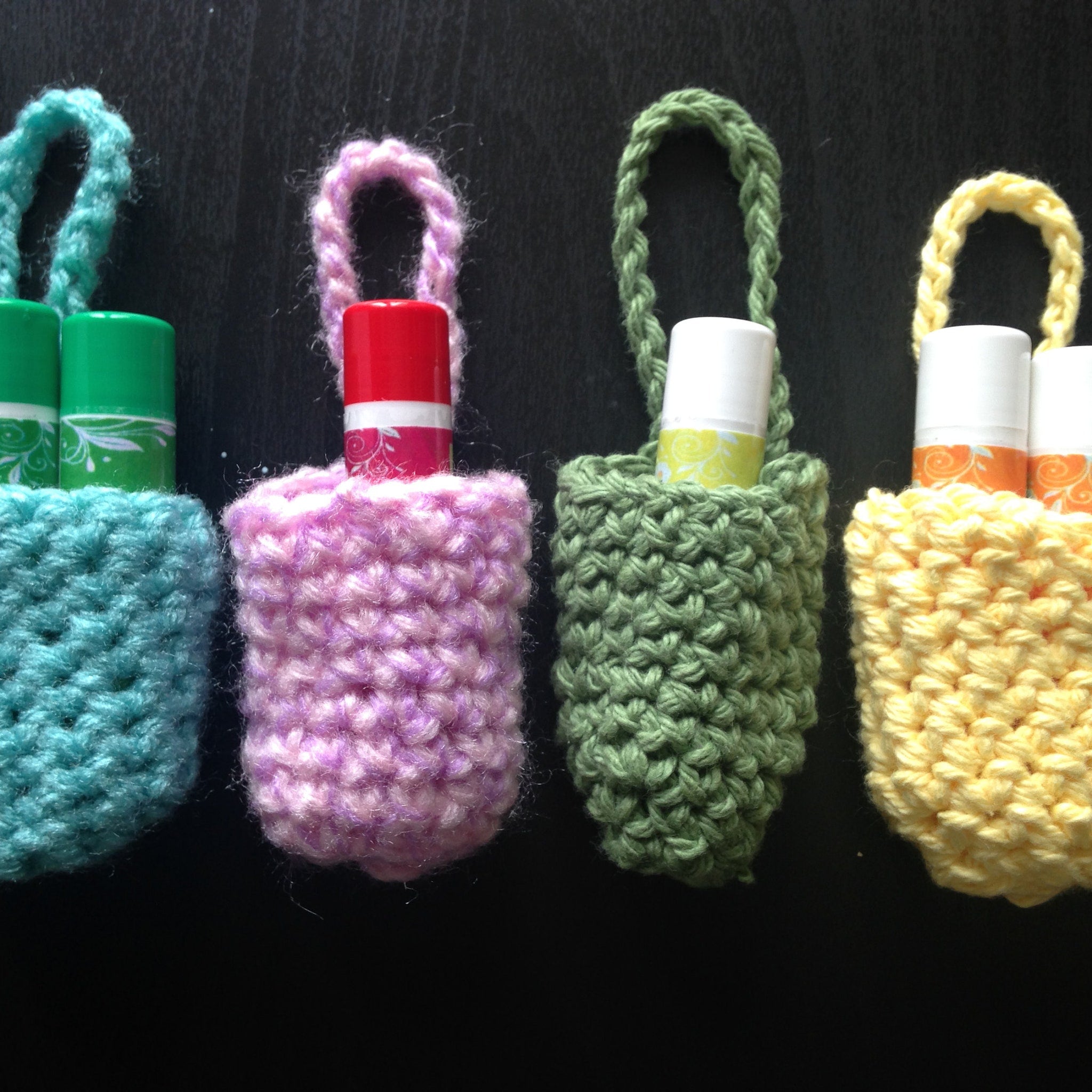 Crocheted lip balm holders in teal, pink, green, and yellow, holding lip balm tubes