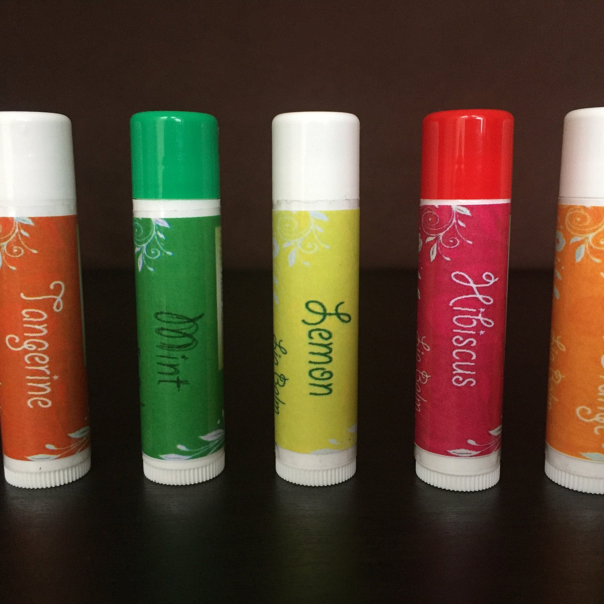 Lip balm tubes in various colors with white tops, patterned labels, and brand text