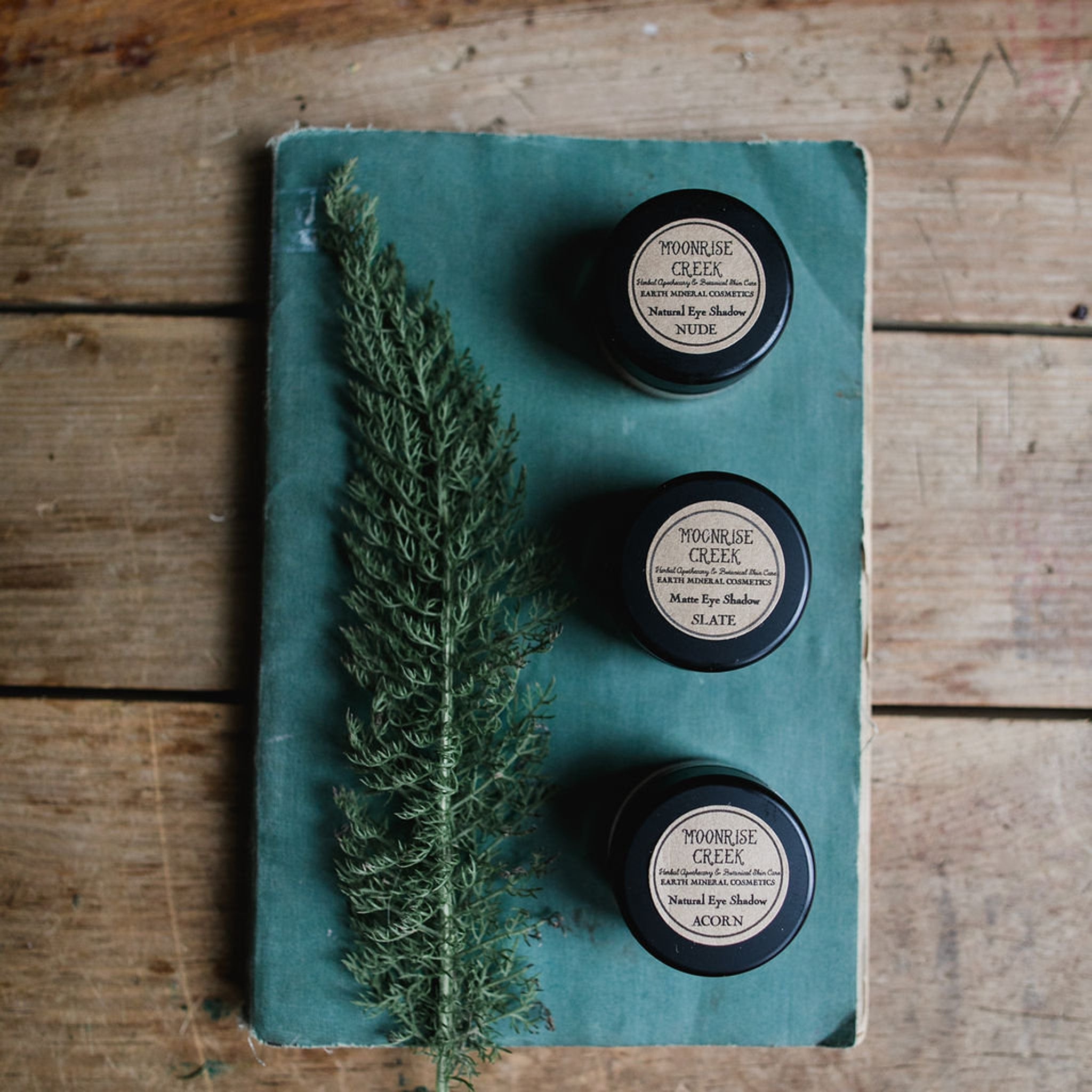 Side view of loose mineral eye shadow powder in glass jar with gold lid, showcasing texture and vegan label details