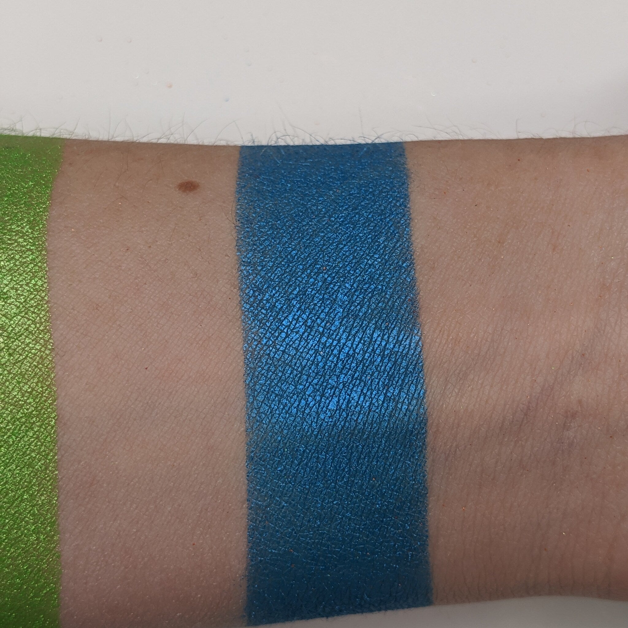 Hand applying teal blue vegan eyeshadow with a brush, showcasing rich pigment and smooth blendability on skin