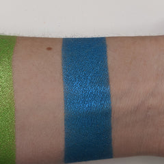Hand applying teal blue vegan eyeshadow with a brush, showcasing rich pigment and smooth blendability on skin