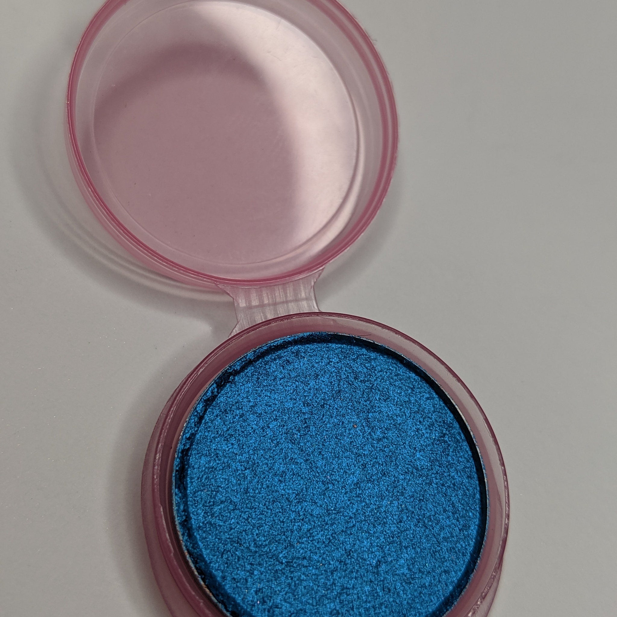 Close-up of vibrant teal blue pressed eyeshadow with smooth matte finish in compact case