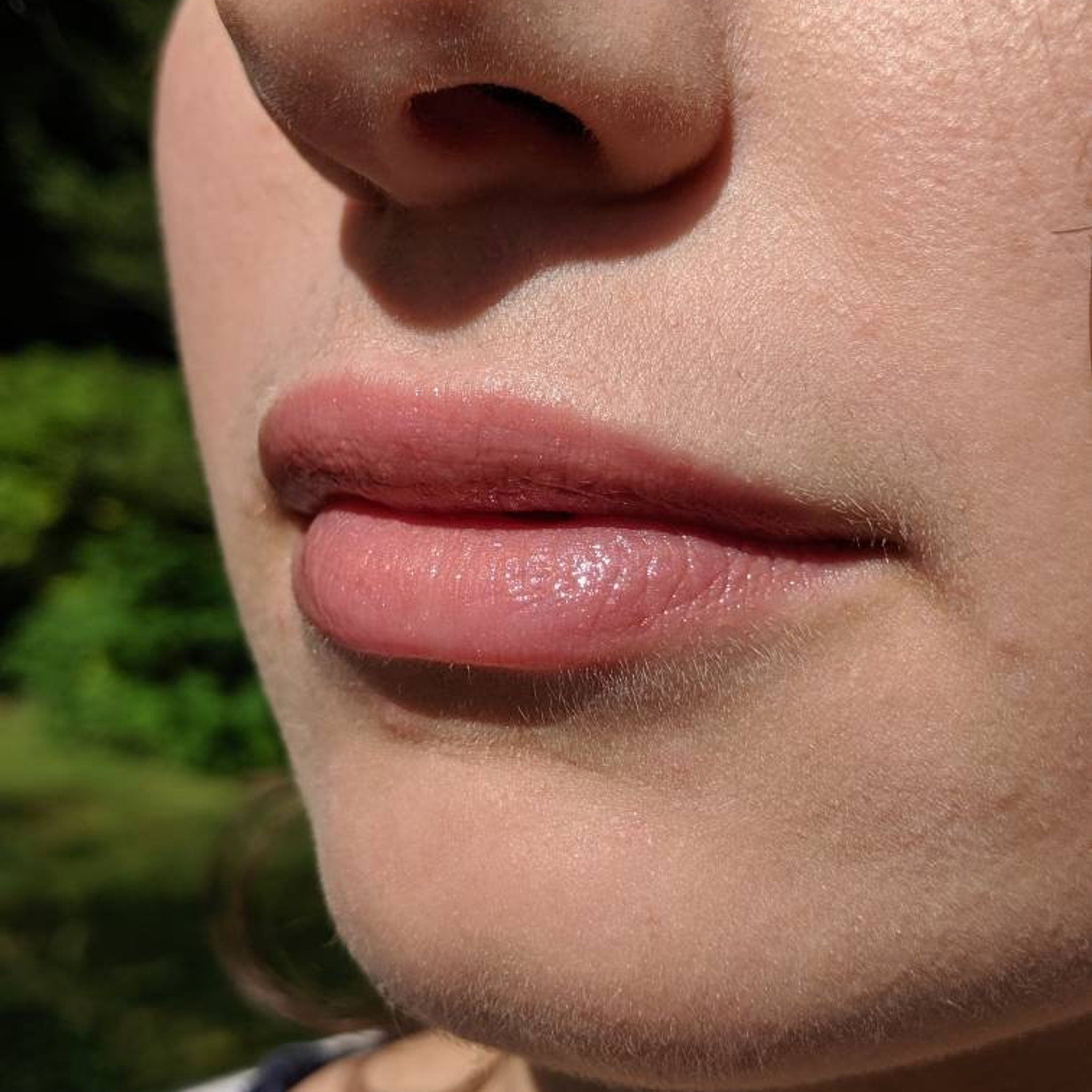 Lip gloss with pink color and glossy finish on lips in natural light