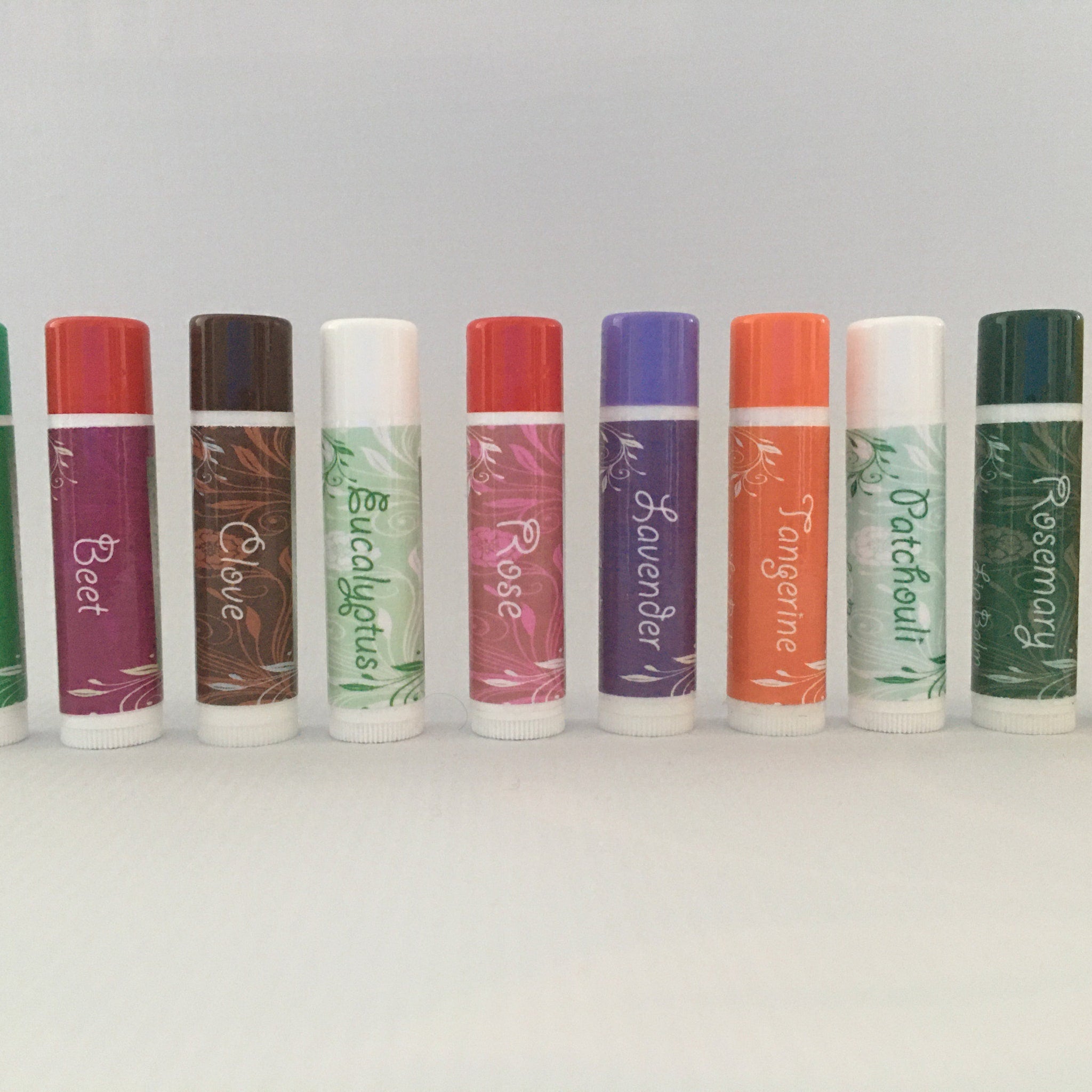 Lip balm tubes with red, purple, and orange caps, floral pattern, and white base